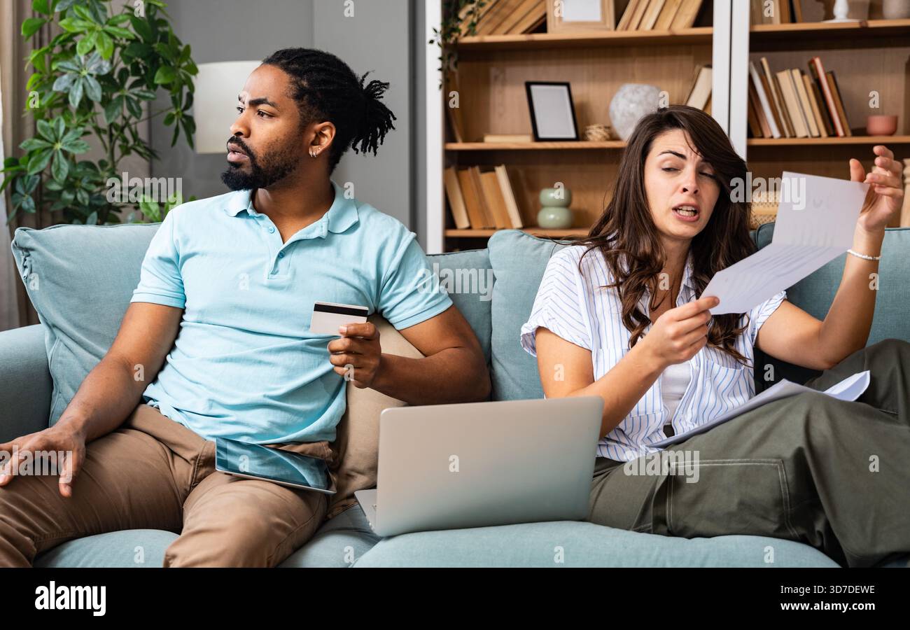 Coppia stressata che esamina le bollette della famiglia che effettuano il pagamento online a casa donna assegno documento mentre l'uomo inserisce i dettagli della carta di debito sul budget del notebook t Foto Stock