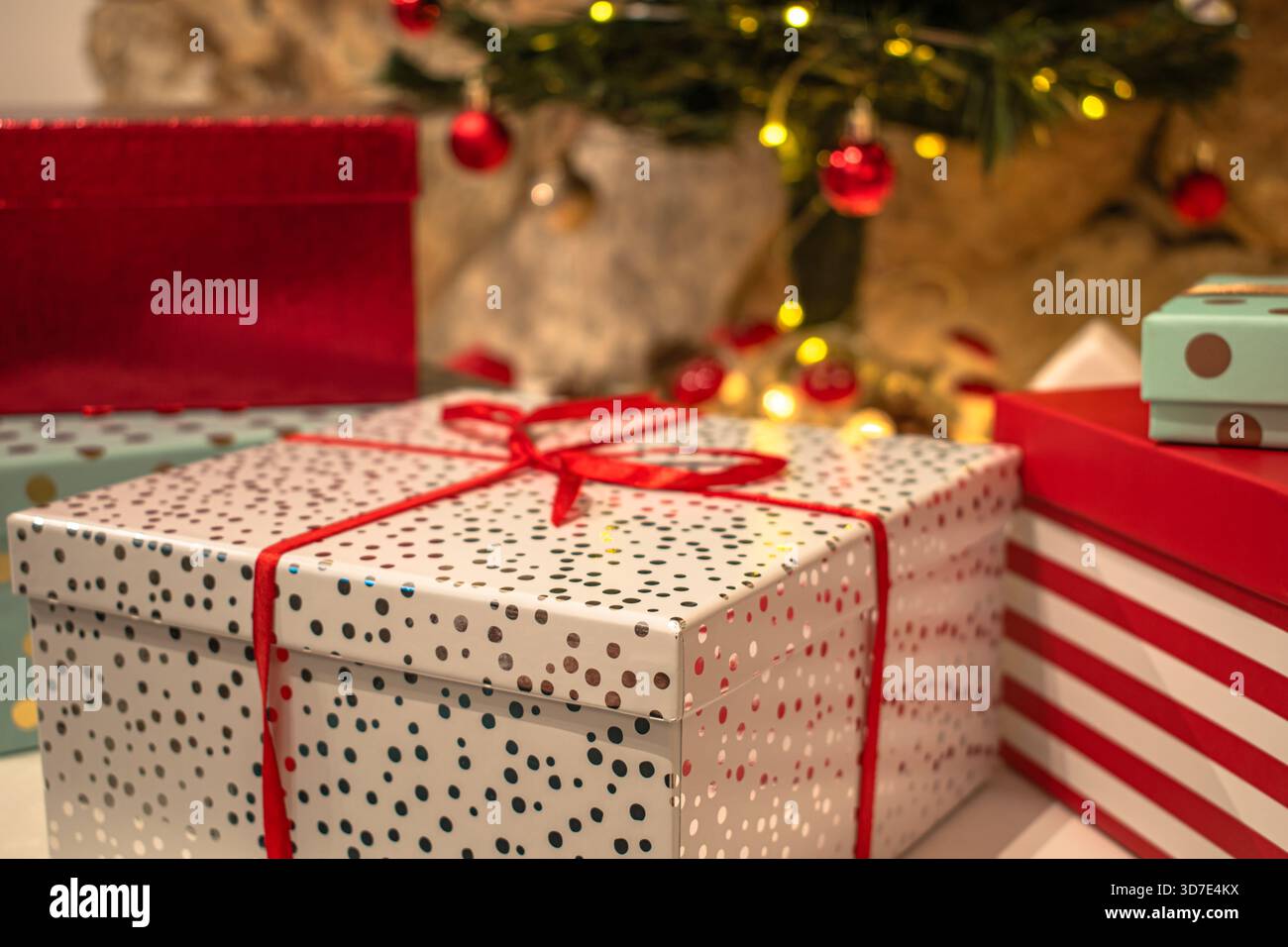 Regali di Natale, scatole luminose con nastri. Una candela e decorazioni natalizie sullo sfondo. Foto Stock
