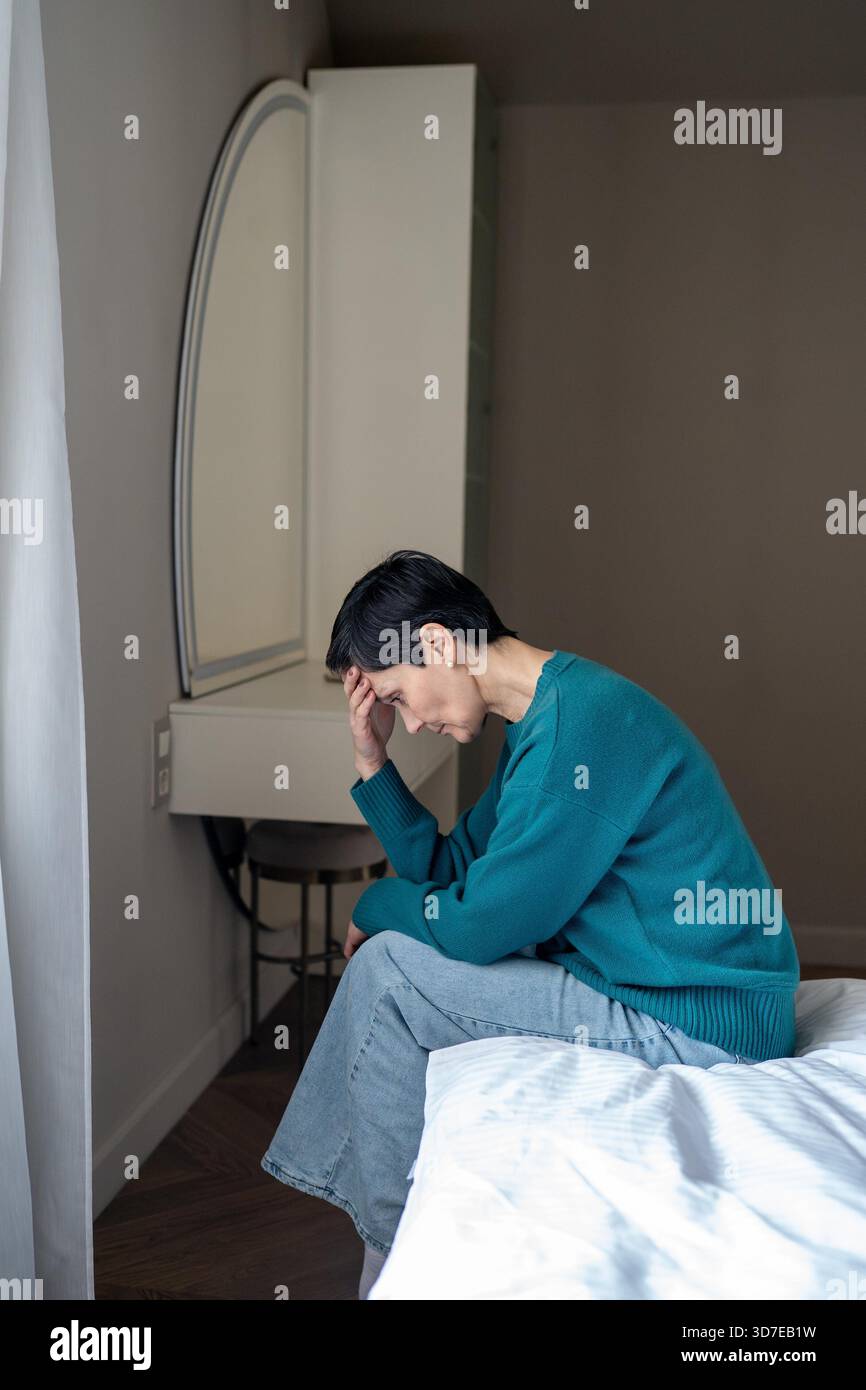 Una donna triste e travolgente disperata sul materasso che guarda verso il basso. Paura delle persone, tensione nervosa, vita isolata, peso psicologico, solitudine di crisi, perdita di interesse, disturbo del sonno cattivo || modello rilasciato Foto Stock