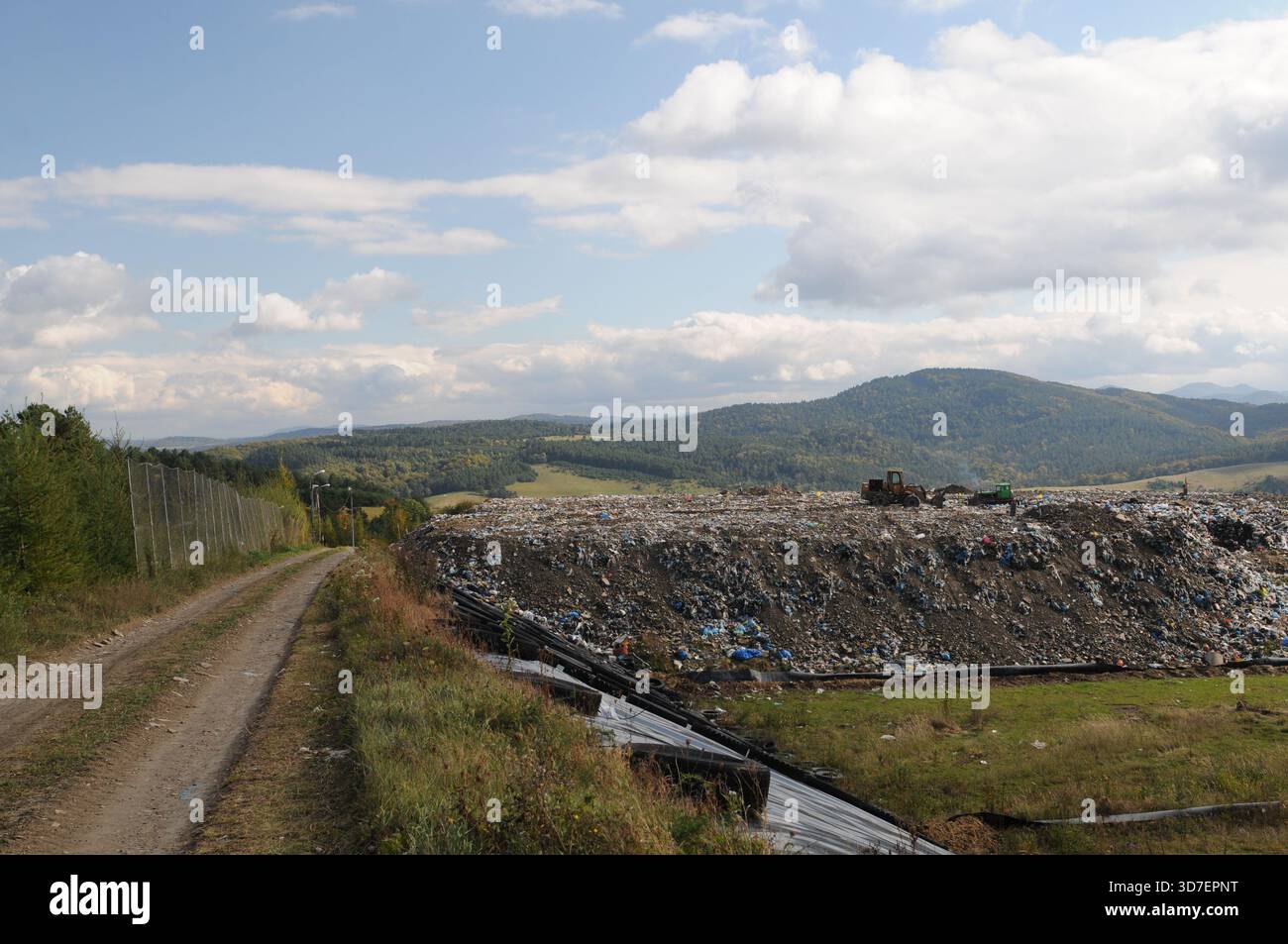 Strada di accesso rurale che conduce a una discarica municipale nella Polonia sudorientale, con cumuli di rifiuti e colline sullo sfondo. Foto Stock