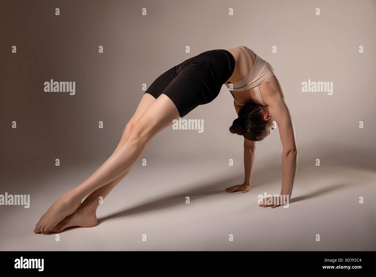 Una donna che esegue un'intensa curvatura posteriore supportata dalle mani, dimostrando flessibilità e forza. Ideale per fitness, pratica yoga e mobilità del corpo Foto Stock