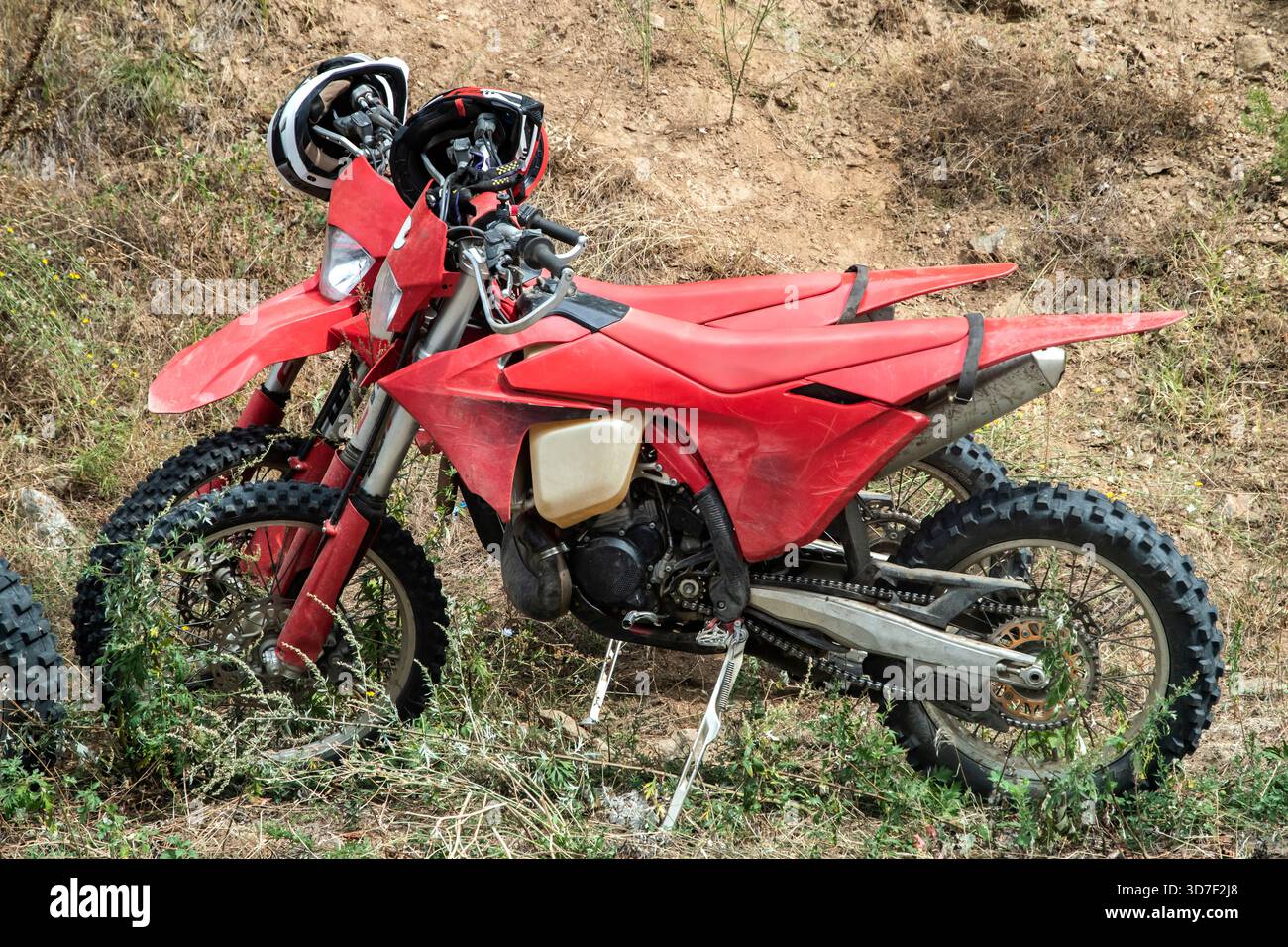 Due motociclette rosse fuoristrada parcheggiate su terreni asciutti con caschi appoggiati sul manubrio in condizioni esterne difficili Foto Stock