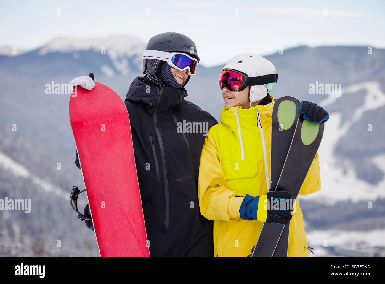 Amici adolescenti sorridenti, snowboarder e sciatore, in piedi insieme sulle piste innevate durante le vacanze invernali, concetto di stile di vita attivo. Foto Stock