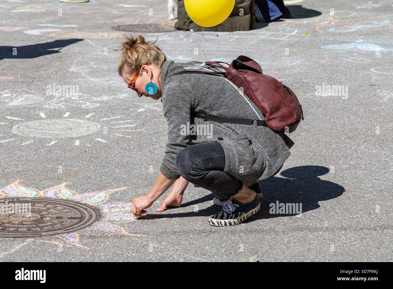 Donna che disegna su un marciapiede con gesso al World Village Festival nel quartiere Suvilahti di Helsinki, Finlandia Foto Stock