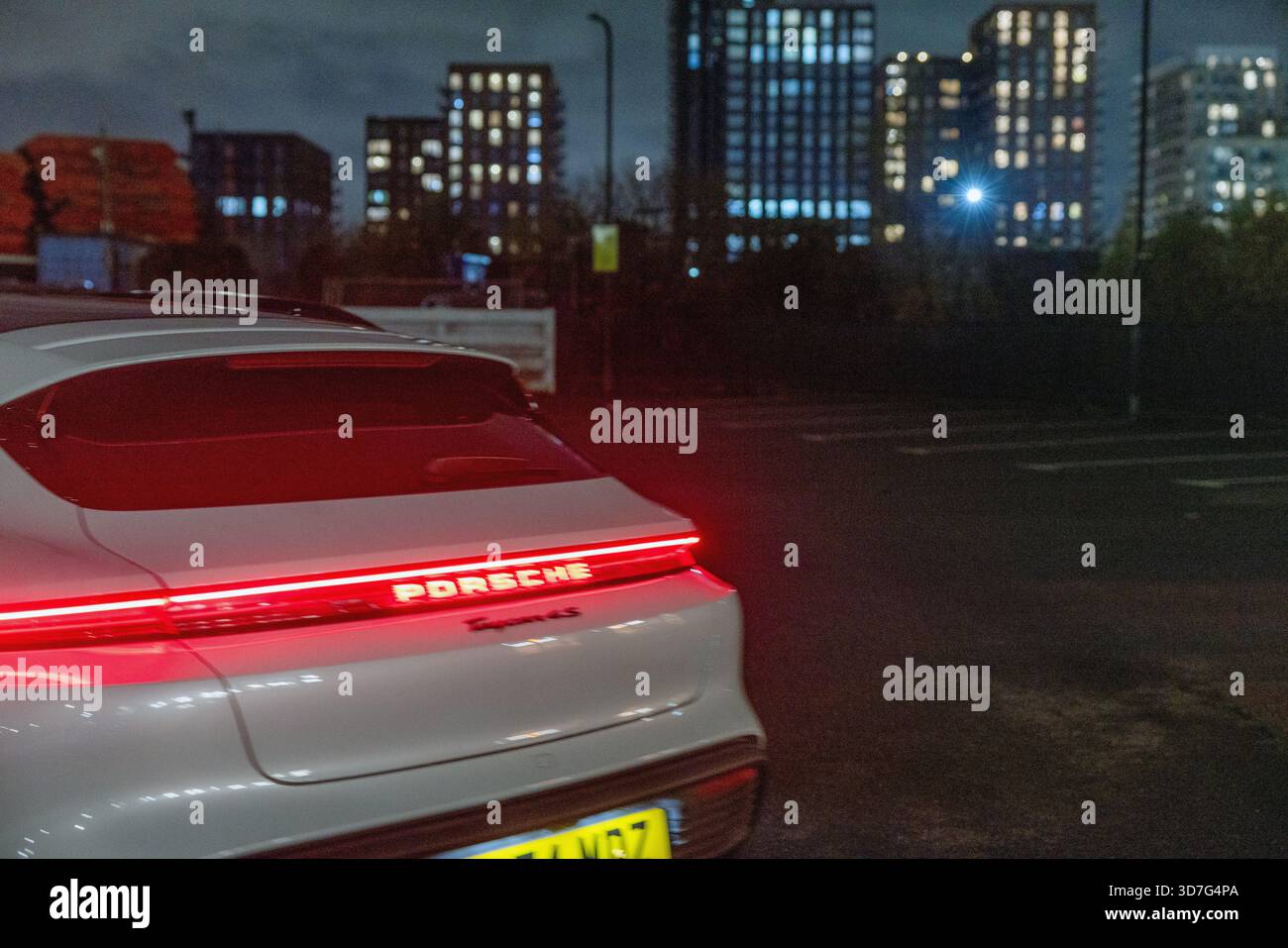 Parte posteriore di un'auto sportiva elettrica Porsche Taycan, che mette in risalto la caratteristica barra luminosa rossa a tutta larghezza con la scritta "Porsche" illuminata. Foto Stock
