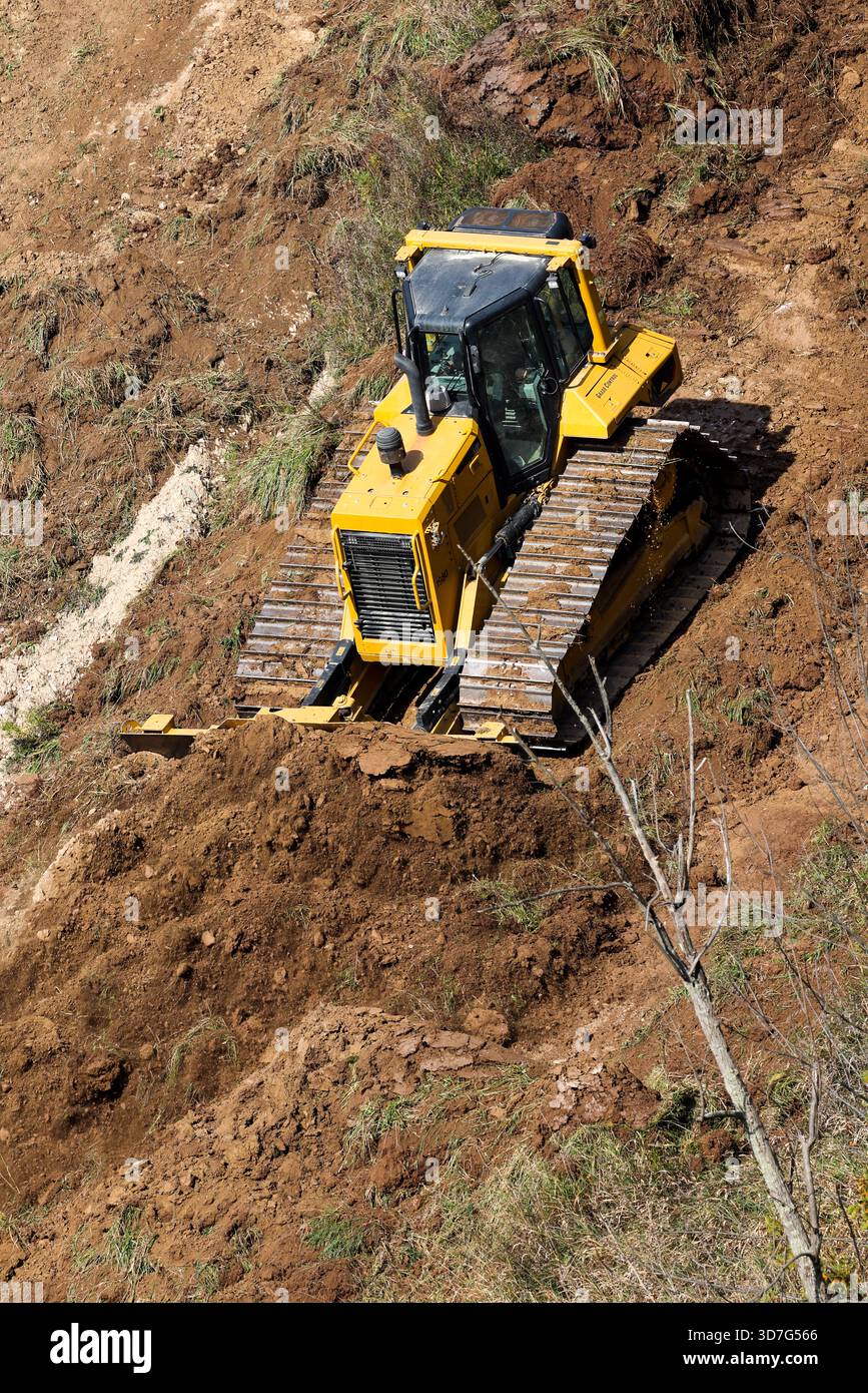 Un bulldozer giallo spinge la terra e il suolo in discesa per rimodellare e intensificare una pista da sci durante i lavori di manutenzione estivi in una stazione sciistica in Canada. Foto Stock