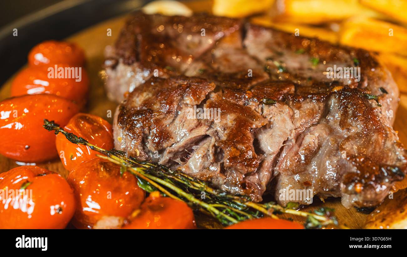 Primo piano di succose costine su tavola di legno con patatine fatte in casa, pomodori ciliegini e timo fresco. Presentazione gourmet, perfetta per il contenuto gastronomico. Foto Stock