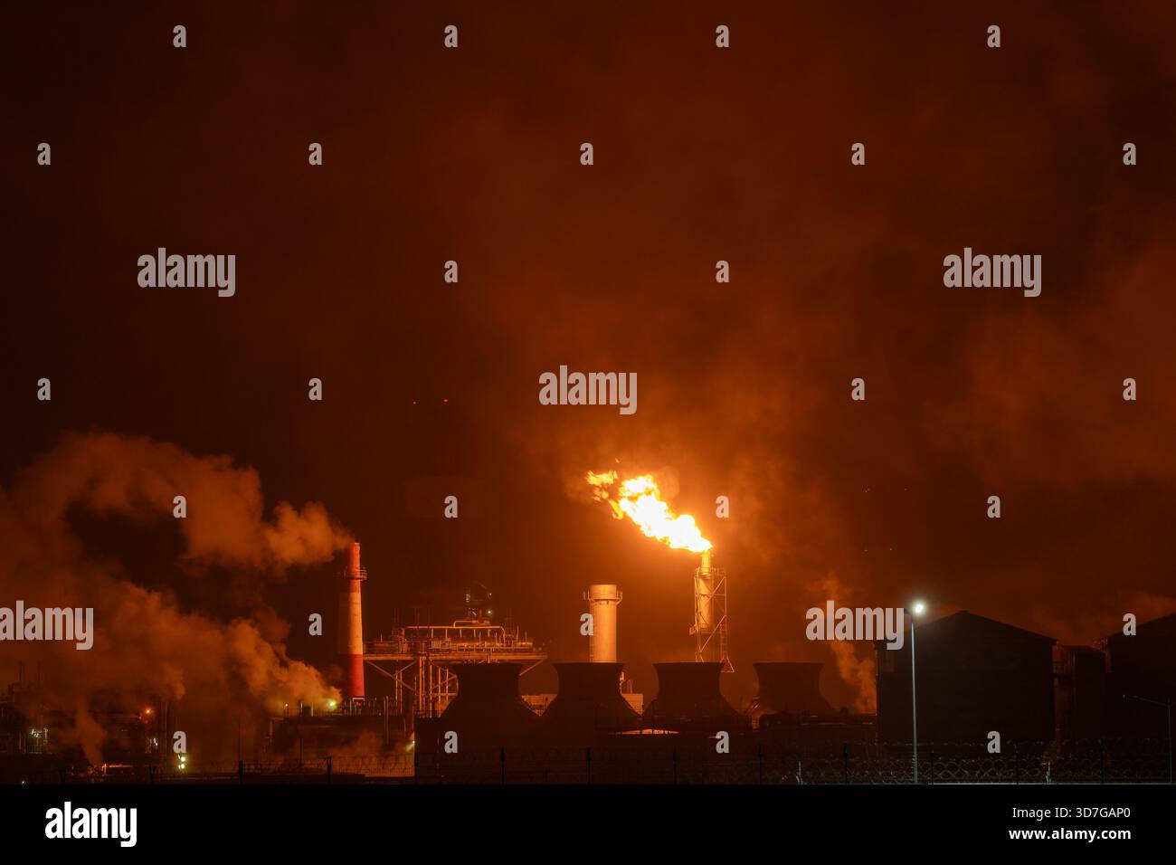 Una pila di luce industriale brucia il gas in eccesso con una grande fiamma arancione brillante e un fumo denso contro un cielo notturno buio, mettendo in evidenza il prodotto energetico Foto Stock