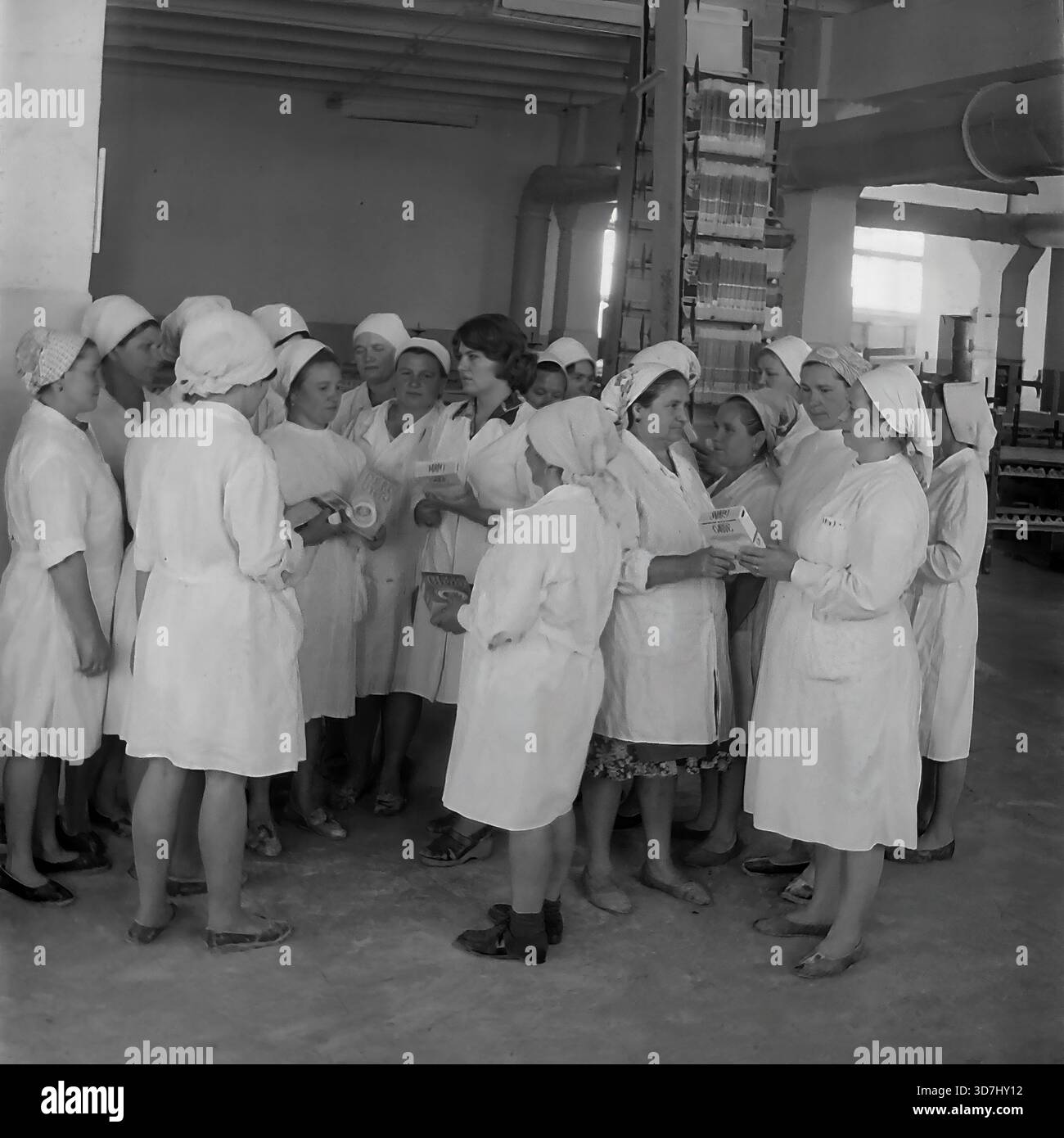 Slaviansk, regione di Donetsk, RSS Ucraina, Unione Sovietica. 1980 anni Una riunione di gruppo di lavoratrici in un'officina di un impianto chimico che produce detergenti sintetici. Le donne con cappotti e velo bianchi si riuniscono in cerchio, tenendo scatole di detersivo in polvere e discutendo della qualità del prodotto. I tubi e le apparecchiature di ventilazione industriale sono visibili sullo sfondo. Questa fotografia d'archivio in bianco e nero cattura lo spirito collettivo e la routine di produzione nella pacifica regione del Donbass molto prima della guerra. Foto Stock