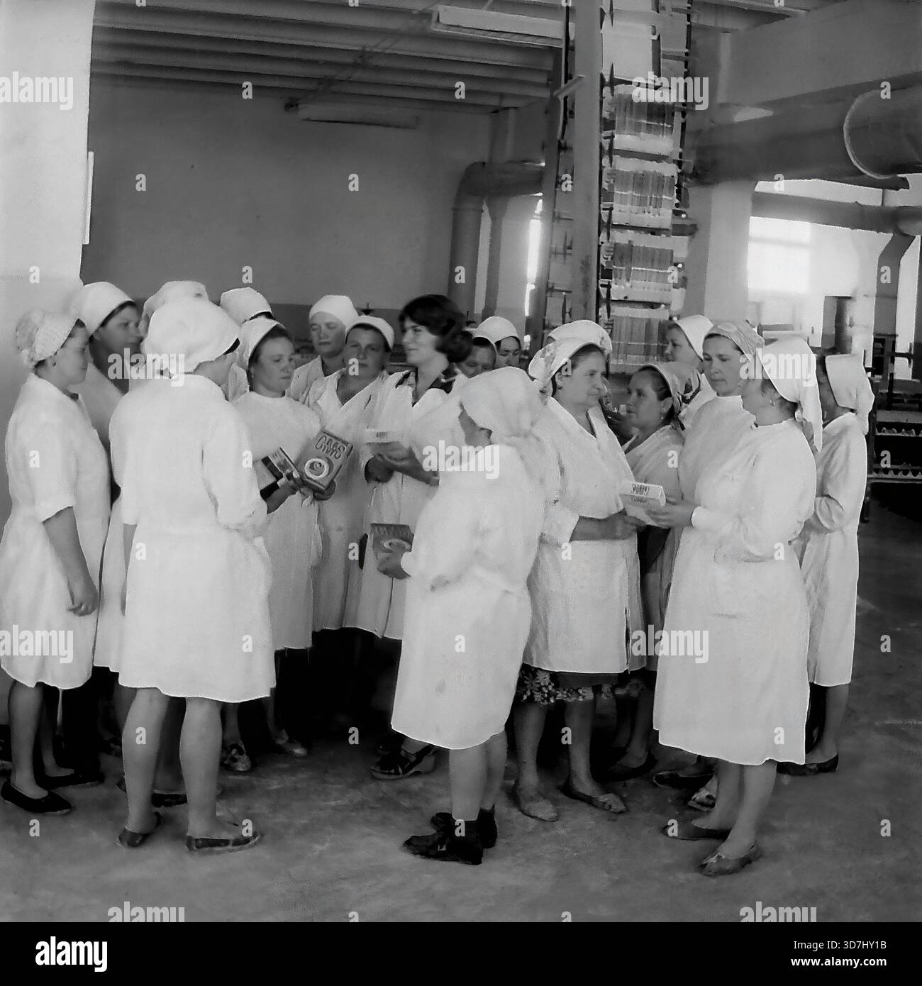 Slaviansk, regione di Donetsk, RSS Ucraina, Unione Sovietica. 1980 anni Una riunione di gruppo di lavoratrici in un'officina di un impianto chimico che produce detergenti sintetici. Le donne con cappotti e velo bianchi si riuniscono in cerchio, tenendo scatole di detersivo in polvere e discutendo della qualità del prodotto. I tubi e le apparecchiature di ventilazione industriale sono visibili sullo sfondo. Questa fotografia d'archivio in bianco e nero cattura lo spirito collettivo e la routine di produzione nella pacifica regione del Donbass molto prima della guerra. Foto Stock