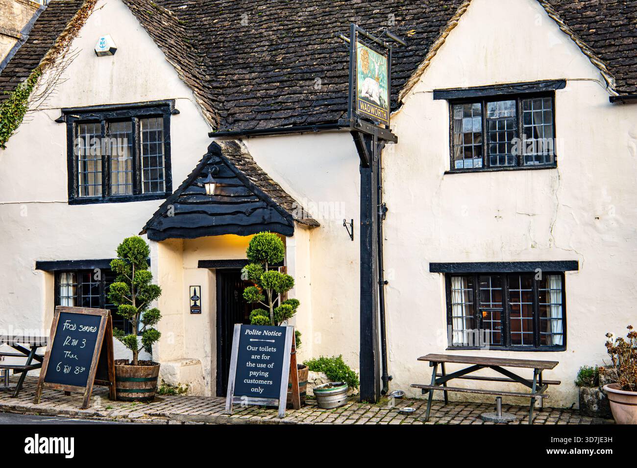 Lo storico pub Castle White Hart, il tetto con cornici in legno e la segnaletica su una strada acciottolata con panche all'aperto e piante in vaso Foto Stock