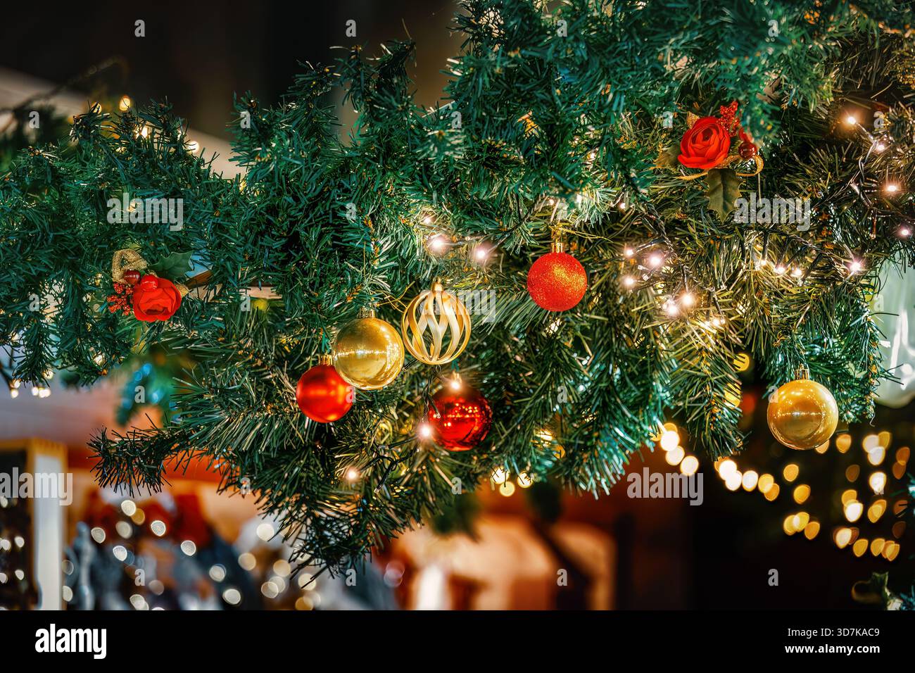 Primo piano di una vivace ghirlanda natalizia adornata da scintillanti baule rosse e dorate e da calde luci scintillanti. Foto Stock