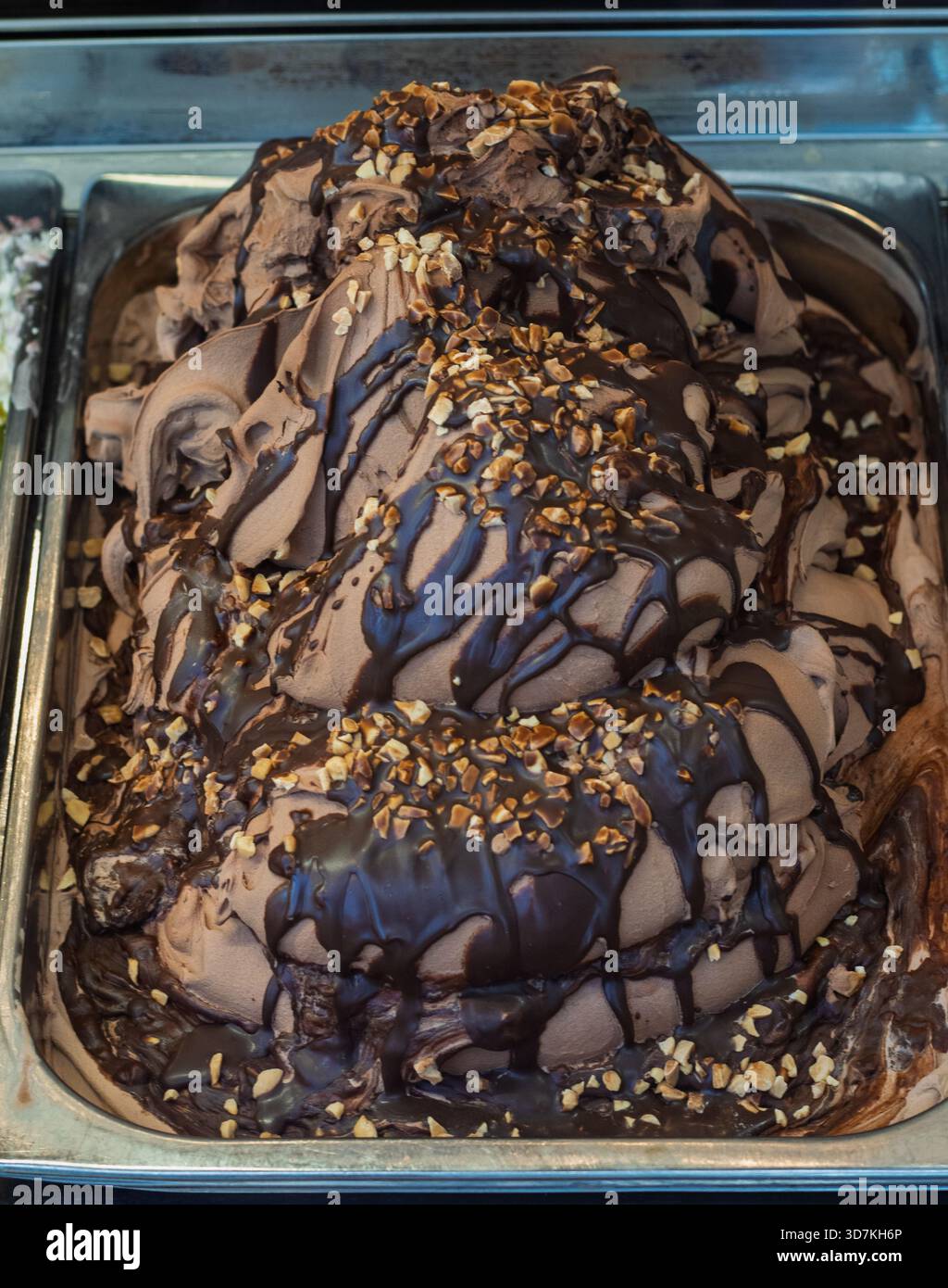 Ricco gelato al cioccolato condito con salsa al cioccolato e nocciole tritate in un contenitore metallico. Un dolce dessert Foto Stock
