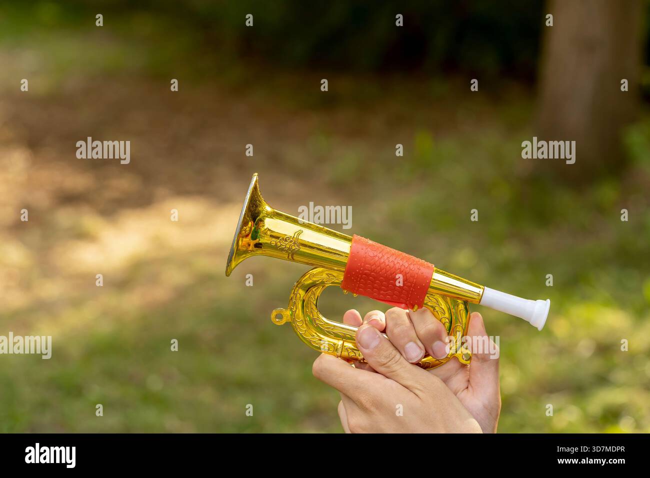 Mani che tengono in mano una tromba rossa giocattolo all'aperto, corno di plastica lucido con finitura oro e boccaglio, fanfa da parata di strumenti musicali per bambini Foto Stock