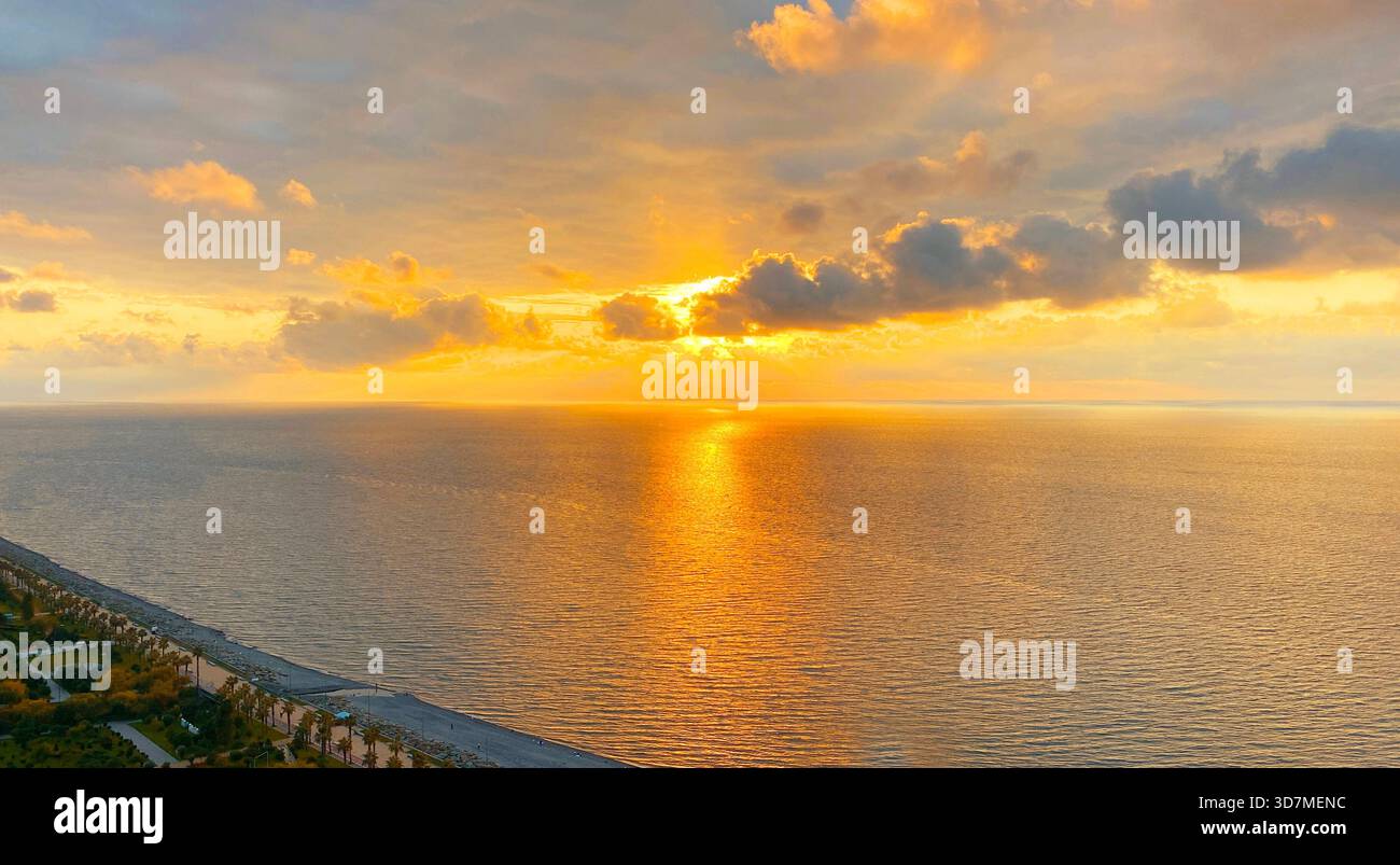 Splendido paesaggio marino, paesaggio costiero marino con spiaggia, cielo e nuvole, un raggio luminoso di sole sull'acqua, increspature al tramonto soleggiato di sera, dorato Foto Stock