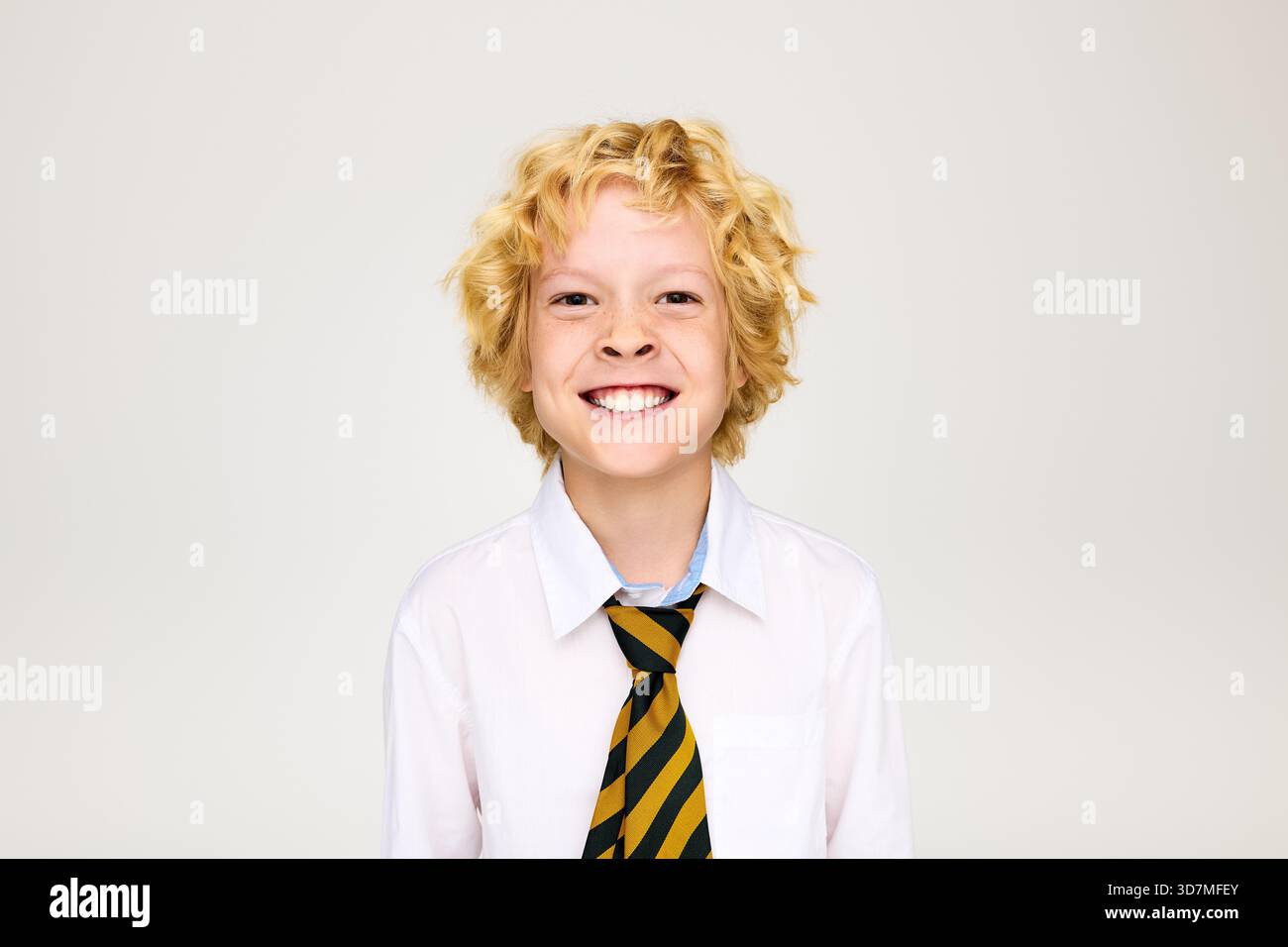 Allegro biondo in uniforme scolastica sorridente in un ambiente da studio. Foto Stock