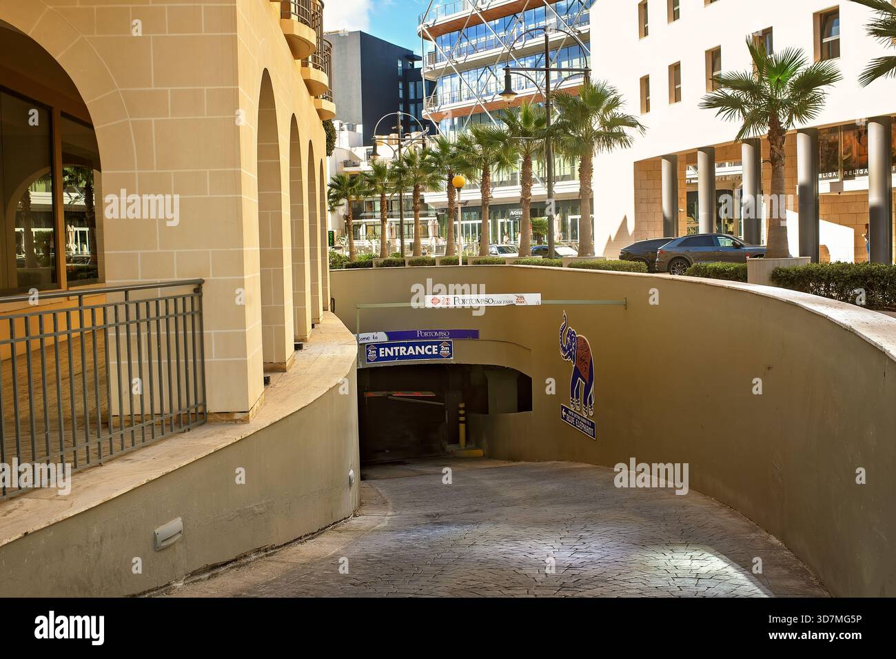 St. Julian's, Malta - 11.11.2025: Ingresso al parcheggio sotterraneo con il ristorante Blue Elephant in una strada soleggiata con palme. Foto Stock