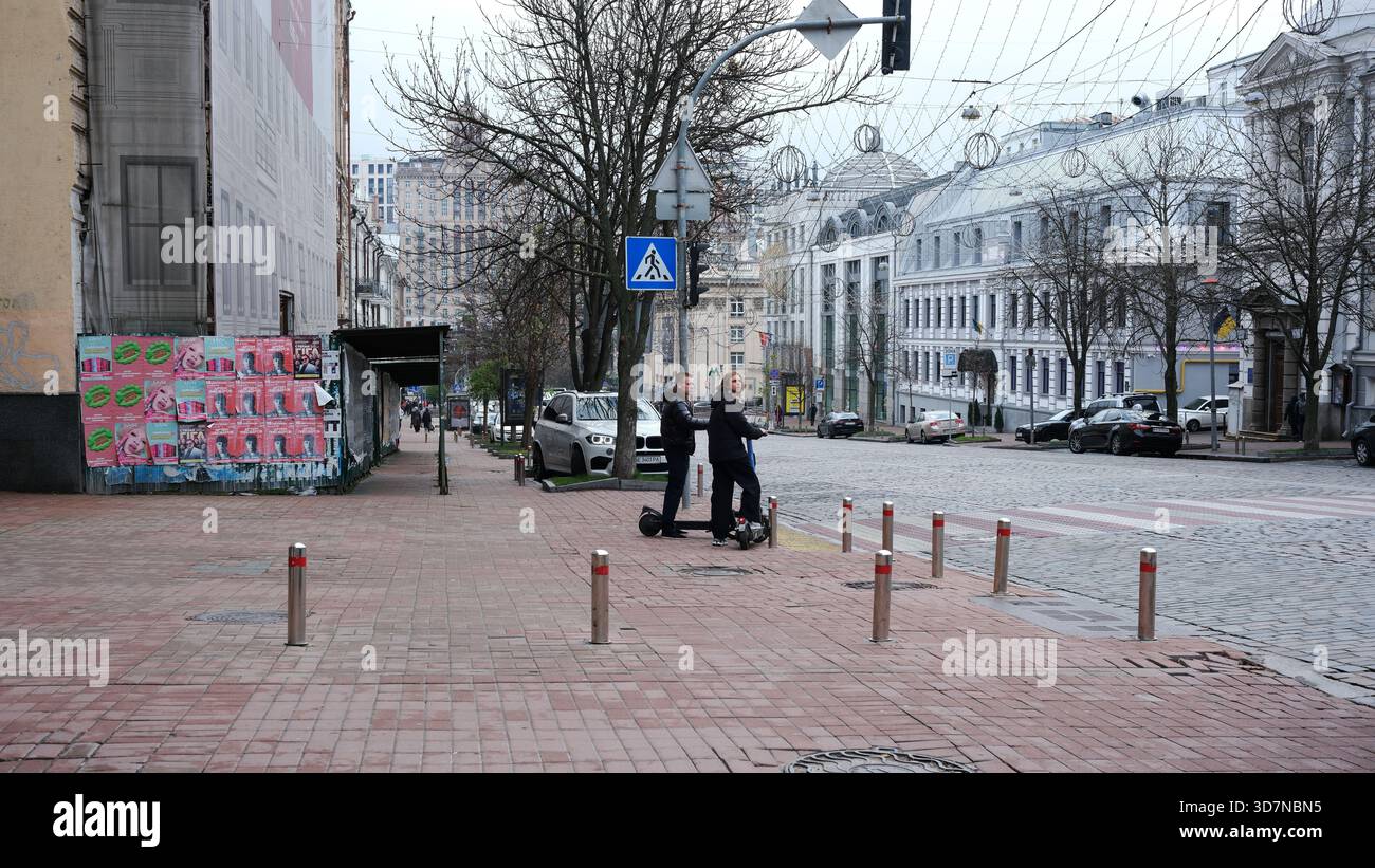 Due amici si divertono a guidare scooter elettrici in una vivace strada della città in inverno. Kiev, Ucraina, 26 novembre 2025. Foto Stock