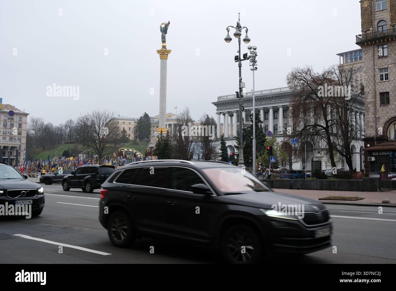 Le auto passano mentre le persone si radunano nella piazza principale della città sotto un cielo grigio. Khreshchatyk, Kiev, Ucraina. 26 novembre 2025. Foto Stock