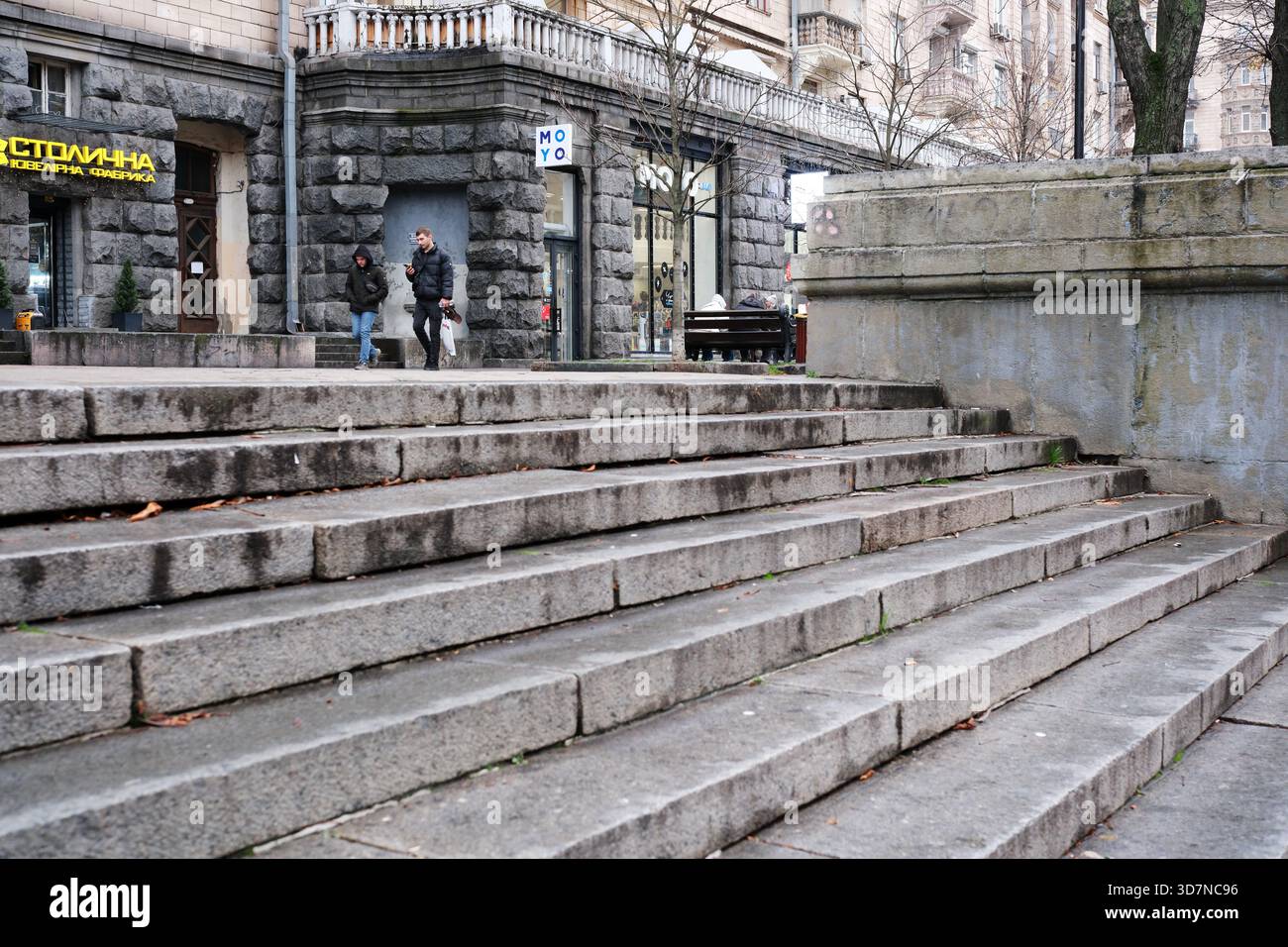 I visitatori passeggiano lungo i gradini di pietra vicino ai negozi di una strada trafficata della città. Khreshchatyk, Kiev, Ucraina. 26 novembre 2025. Foto Stock