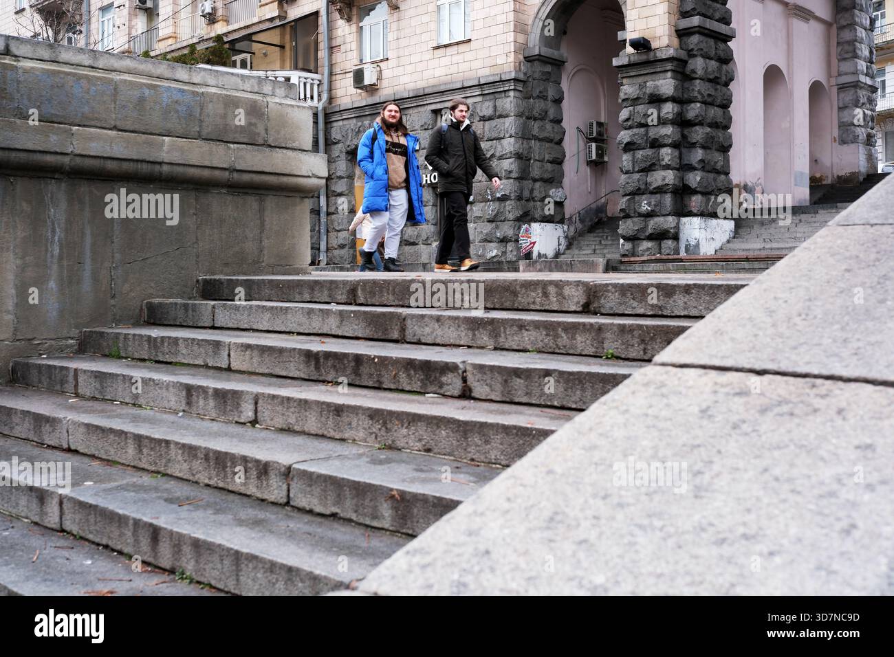 Due amici camminano giù per scalini di pietra in una città, condividendo un momento di risate e gioia. Khreshchatyk, Kiev, Ucraina. 26 novembre 2025. Foto Stock