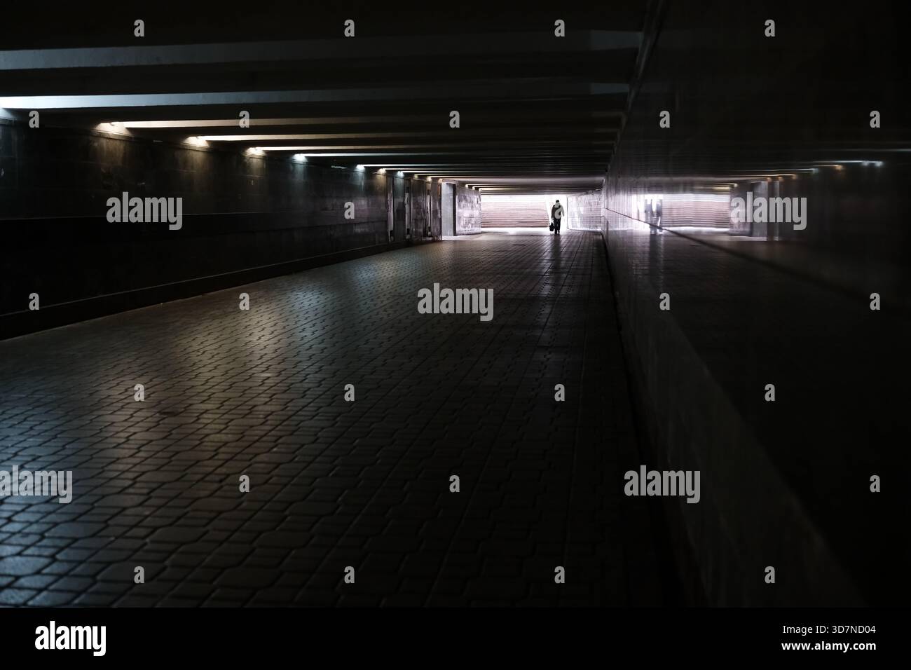 Una figura solitaria percorre un tunnel deserto illuminato da una luce delicata. Foto Stock