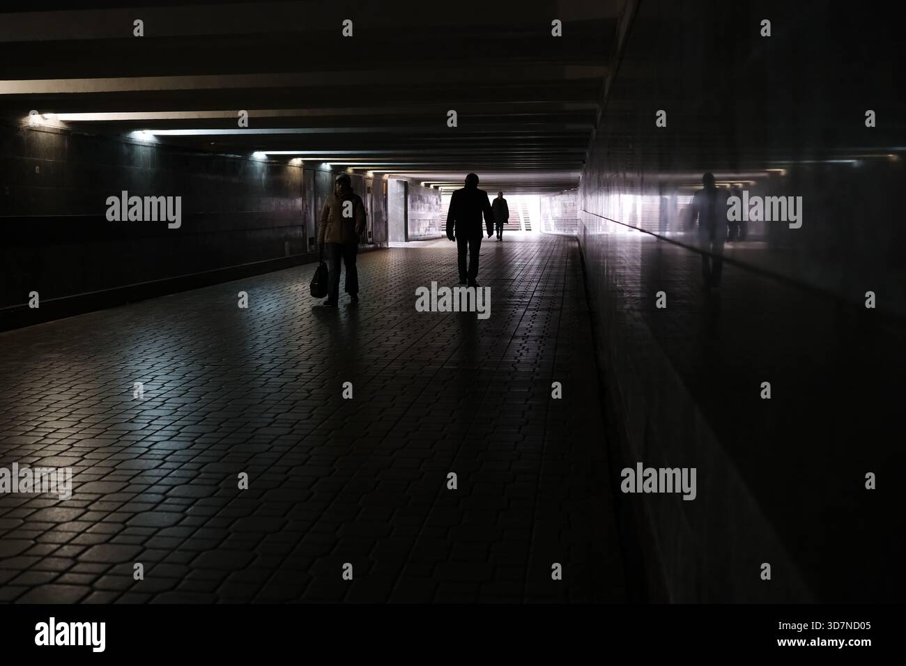 Due figure passeggiano attraverso un tunnel oscuro, illuminato da luci soffuse. Foto Stock