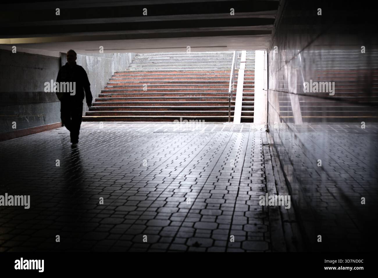 Una figura solitaria cammina attraverso un tunnel buio verso una luce soffusa all'esterno. Foto Stock