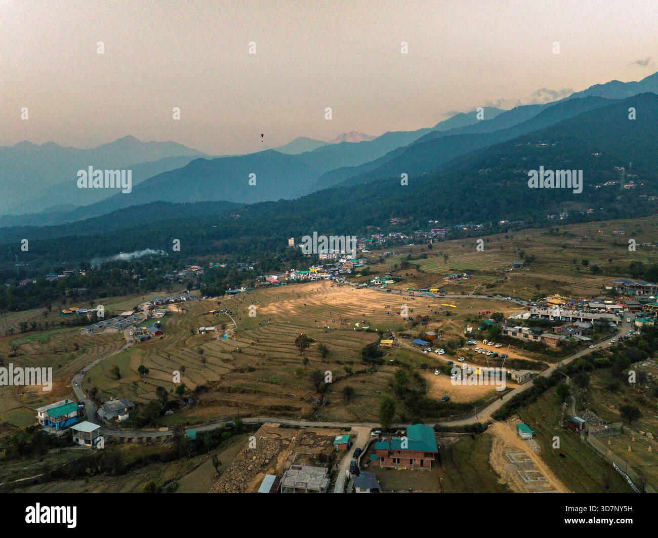 Vista aerea della luce del sole dorata che baciano i campi terrazzati mentre illumina la città annidata contro le maestose montagne tinto di blu, Baijnath e Himac Foto Stock
