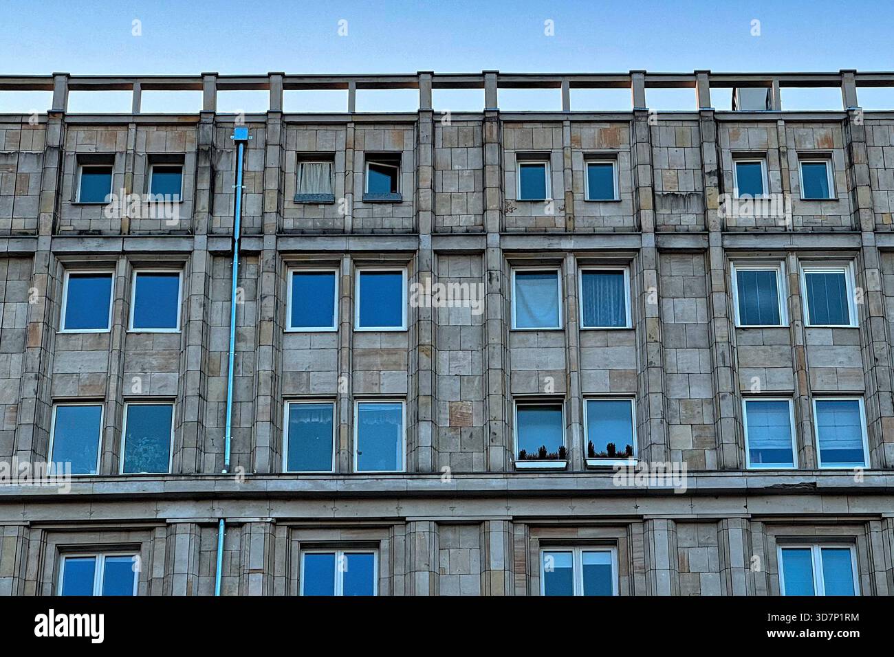 Grandiosa facciata di un edificio di epoca comunista con finestre ripetitive e forti linee architettoniche contro un cielo limpido, che mostra la storia della città Foto Stock