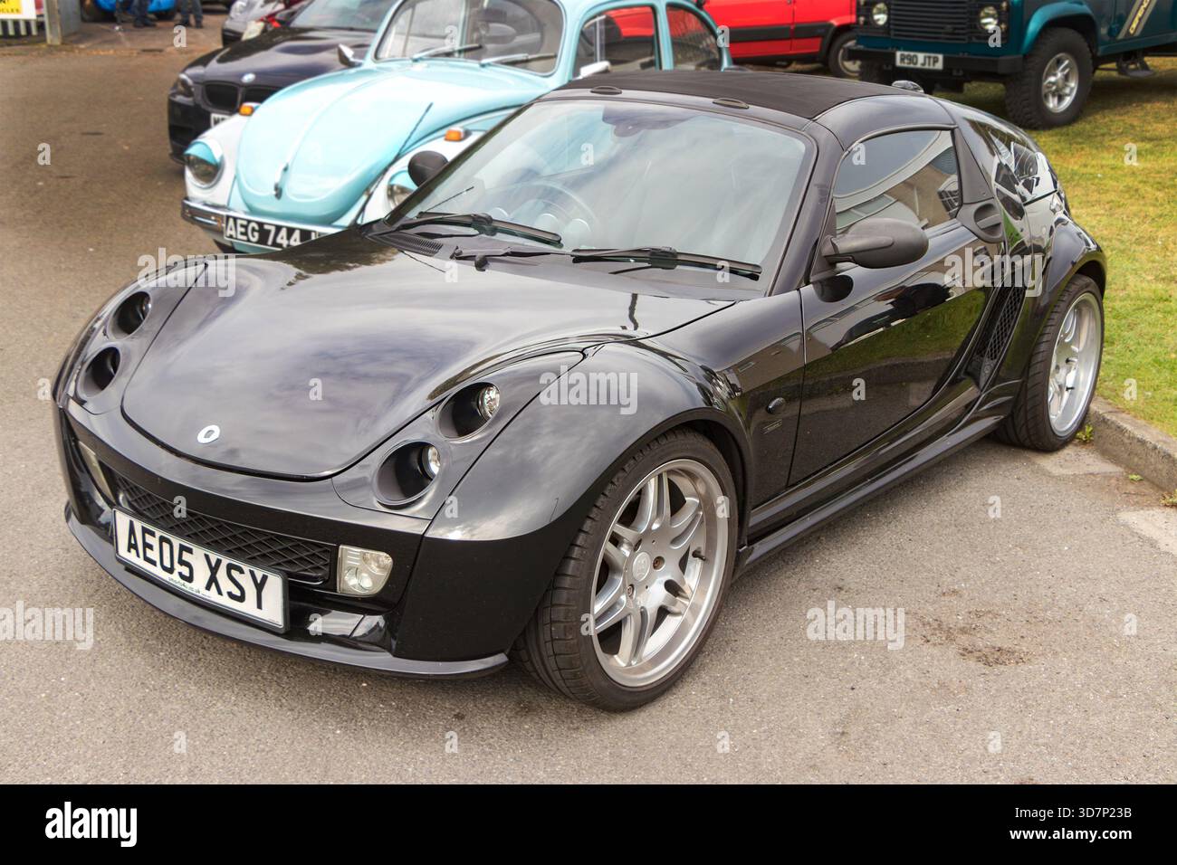 La Black Smart Roadster Coupe parcheggiata in una mostra automobilistica con auto d'epoca, tra cui un Maggiolino Volkswagen azzurro sullo sfondo Foto Stock