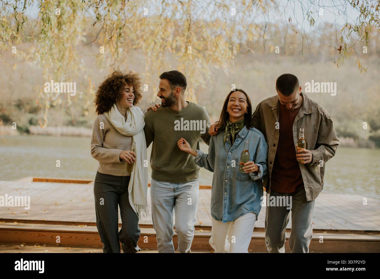 Un gruppo di amici affiatato festeggia sul lago, ridendo e condividendo bevande sotto un cielo soleggiato, godendosi la natura insieme. Foto Stock