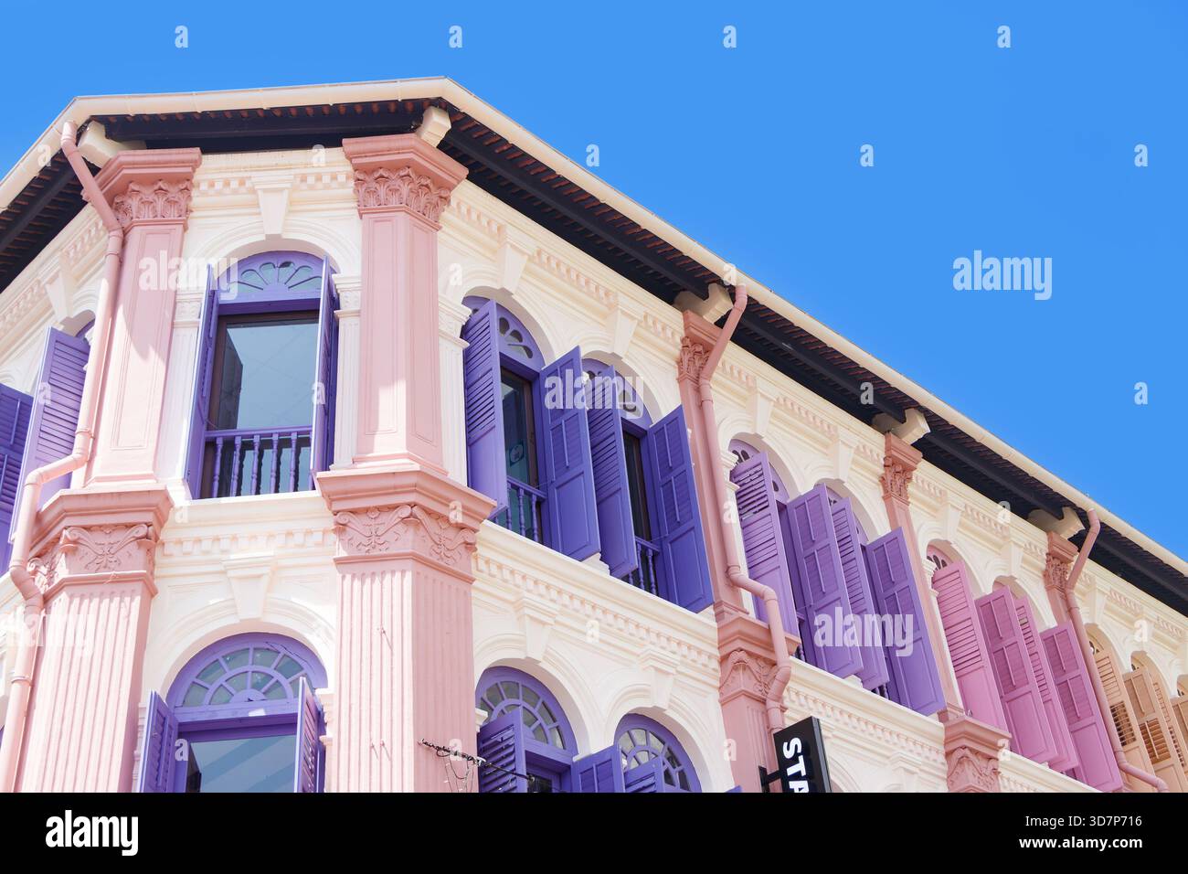 Edificio colorato in stile coloniale con finestre ad arco e persiane pastello in rosa, viola e bianco sotto un cielo limpido e vibrante singapore Foto Stock