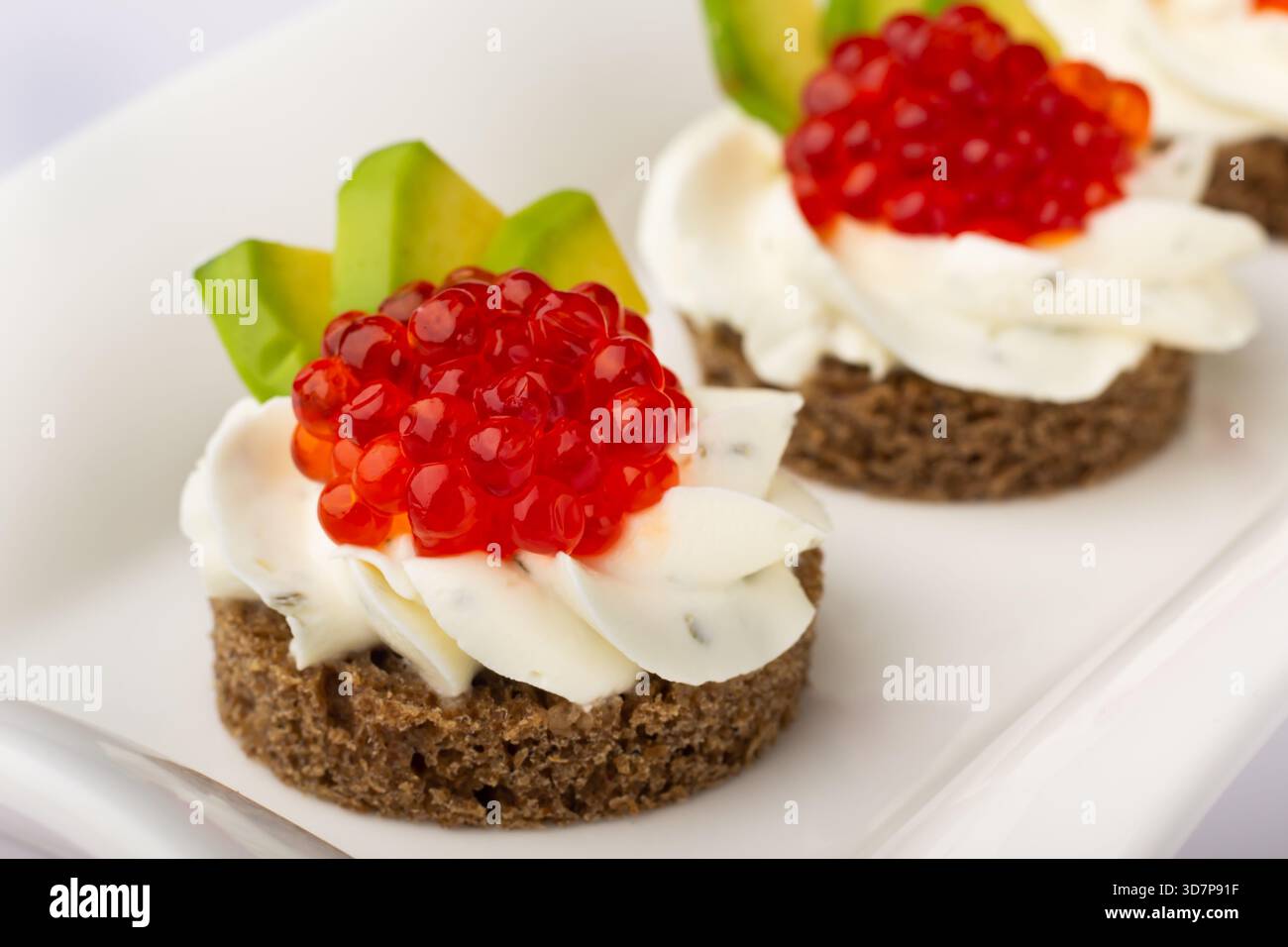 Questi tartine sono caratterizzati da una base di pane scuro, ricoperto da cremosa spalmazione e vivace caviale rosso, guarnito con avocado Foto Stock