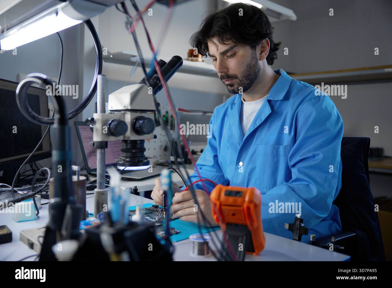 Il tecnico si è impegnato attivamente in lavori critici sulla scheda a circuiti stampati osservando al microscopio Foto Stock