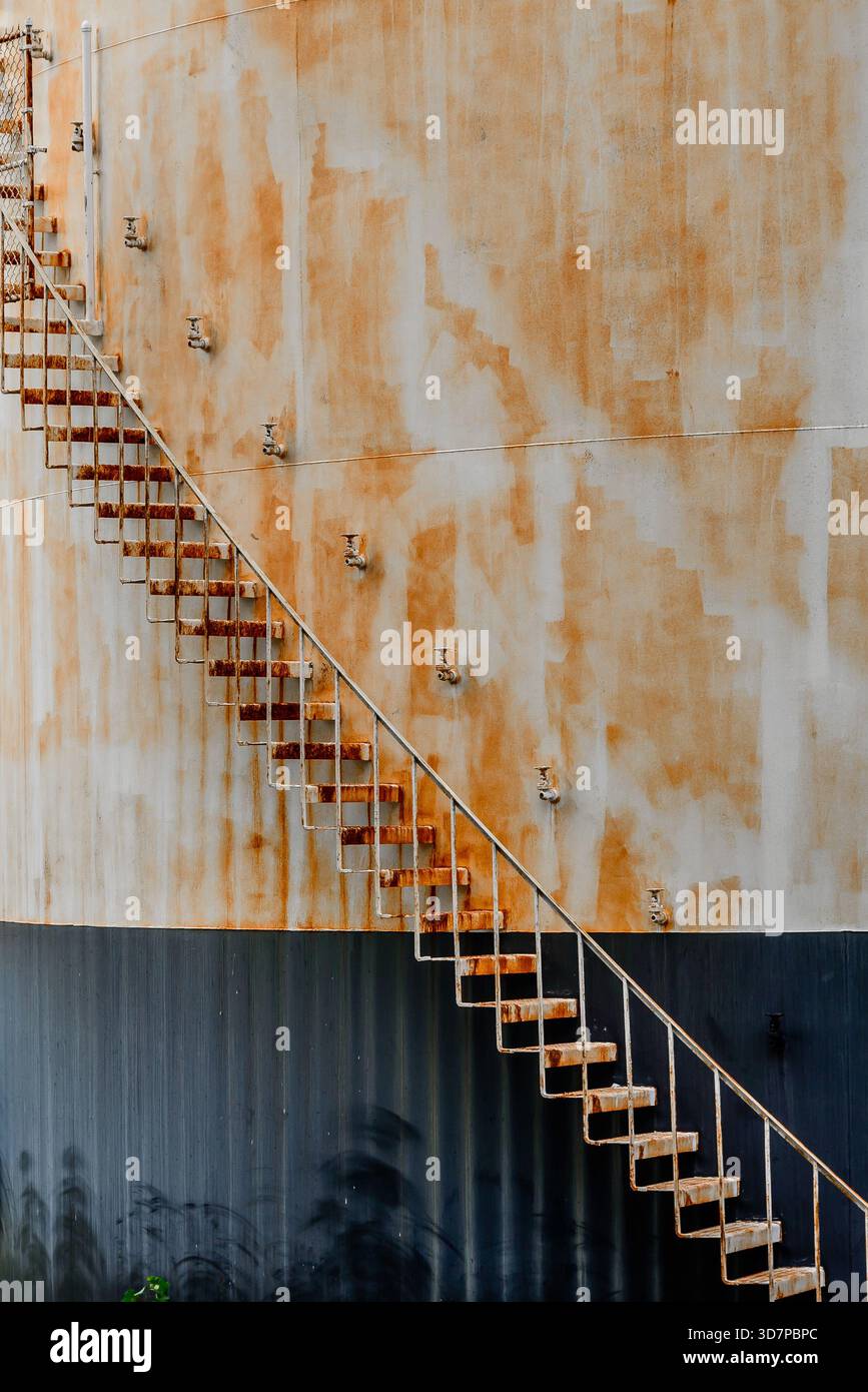 Le scale arrugginite girano attorno a un serbatoio arrugginito. Foto Stock