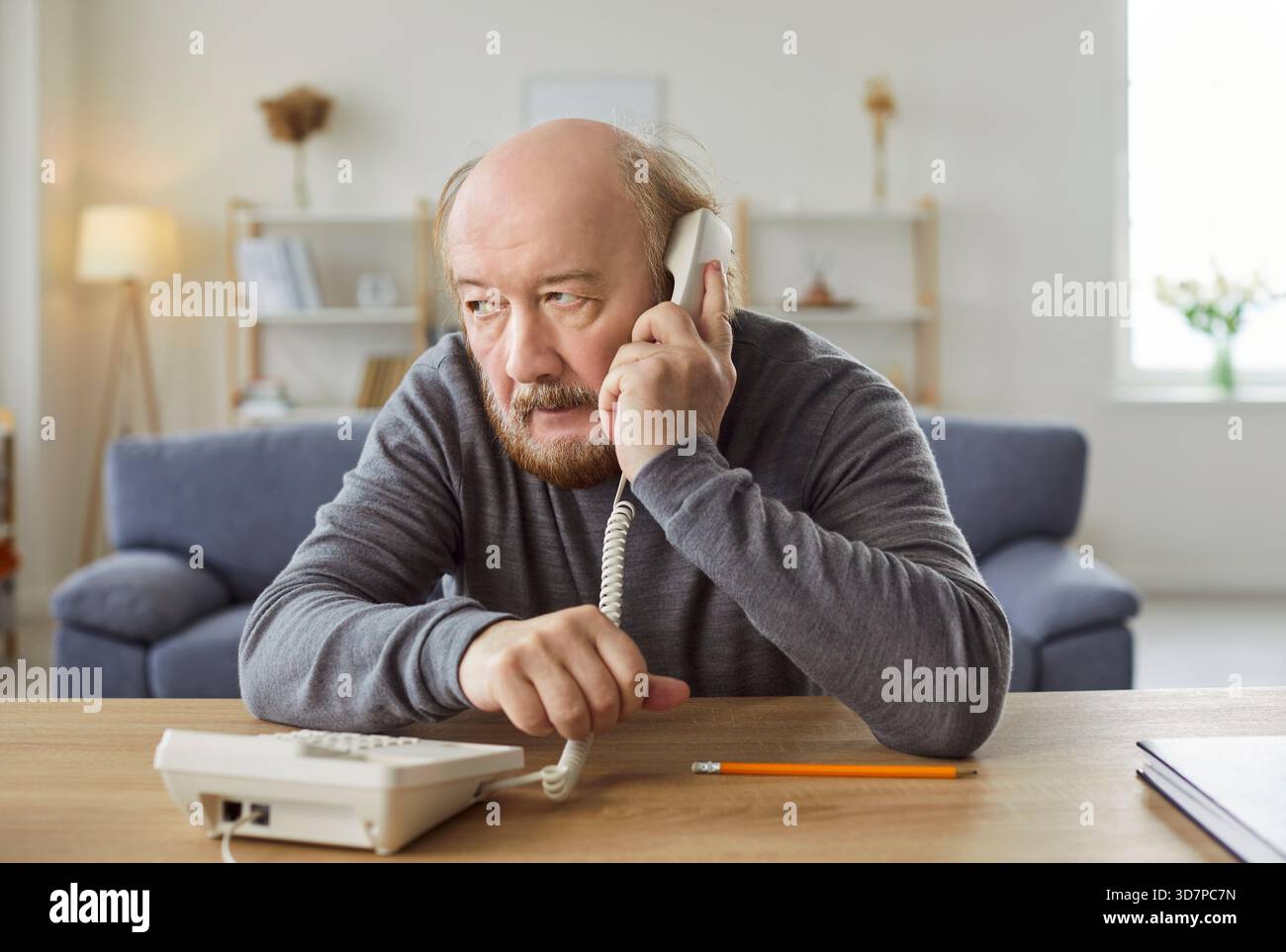 Uomo serio e maturo che parla, tiene il ricevitore vicino all'orecchio, effettua una chiamata telefonica Foto Stock