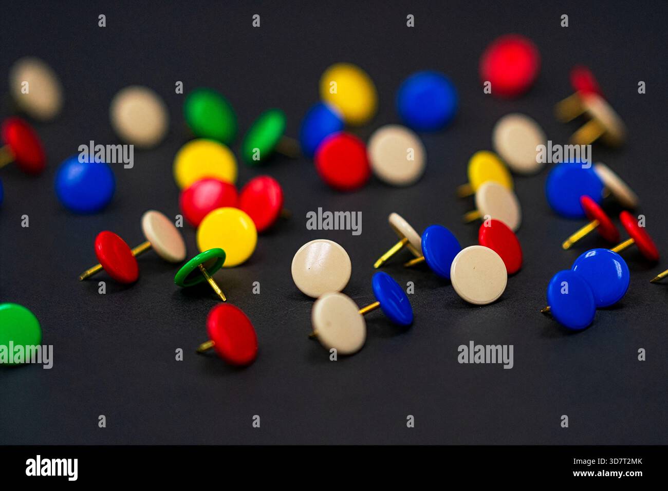 Una dispersione di miniature colorate (pulsanti) in rosso, blu, verde e beige su una superficie nera, con una profondità di campo bassa. Foto Stock