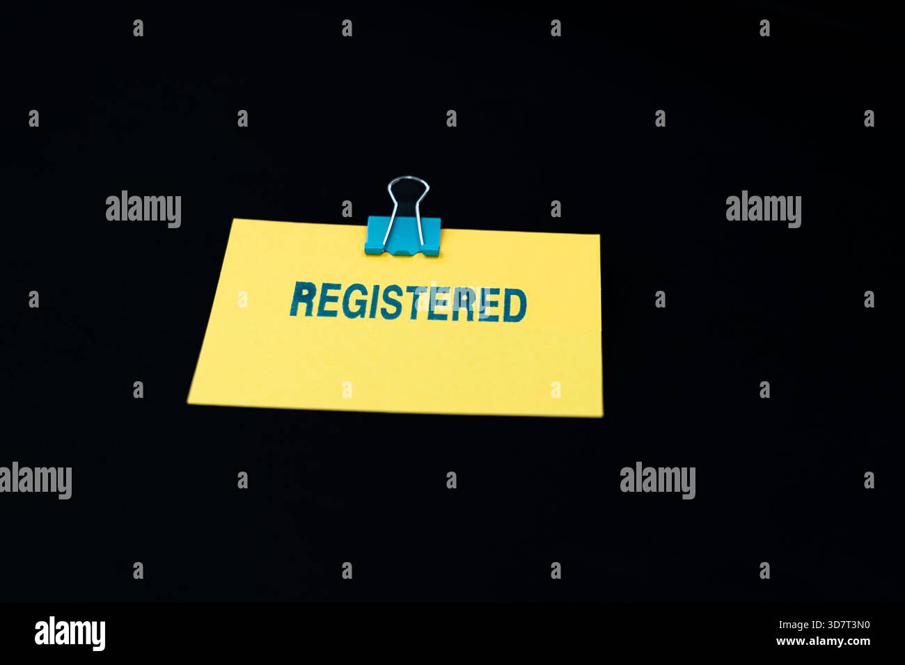 Una nota adesiva gialla brillante mostra la parola "REGISTRATO" stampigliata in blu, su uno sfondo nero intenso. Foto Stock