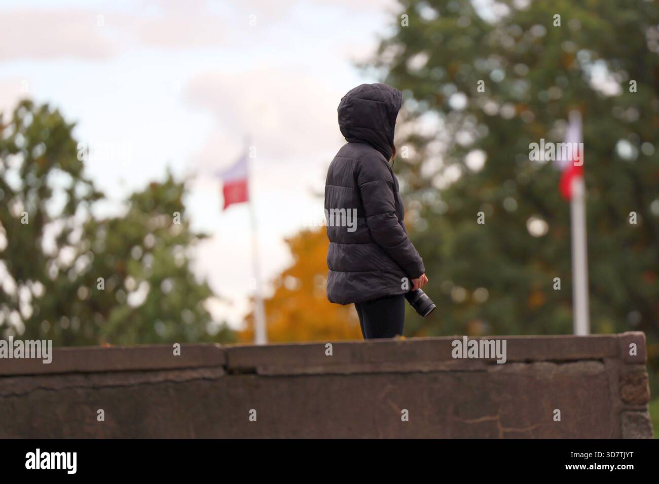 Fotografo in giacca con cappuccio che cattura paesaggi autunnali con bandiere lucide Foto Stock
