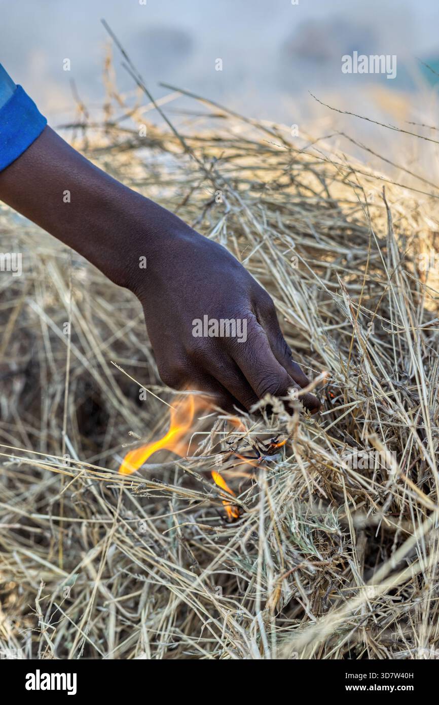 uomo africano che accende l'erba secca, pratica la combustione culturale o la combustione fredda nella gestione tradizionale del territorio Foto Stock