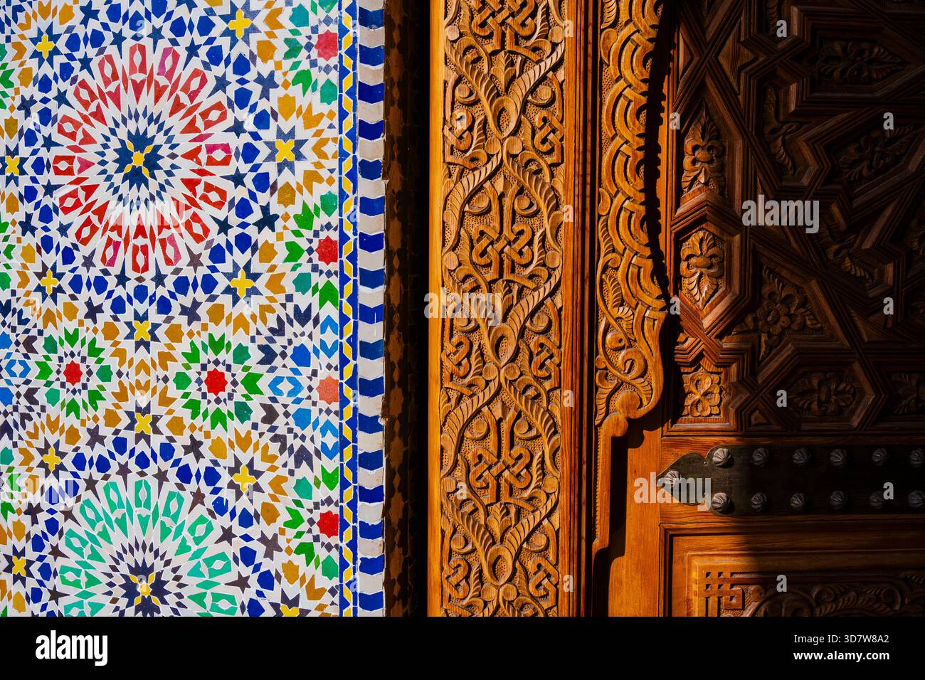 Intricate piastrelle a mosaico accanto a sculture in legno ornate in una vibrante luce del sole. Marrakech, Marocco Foto Stock