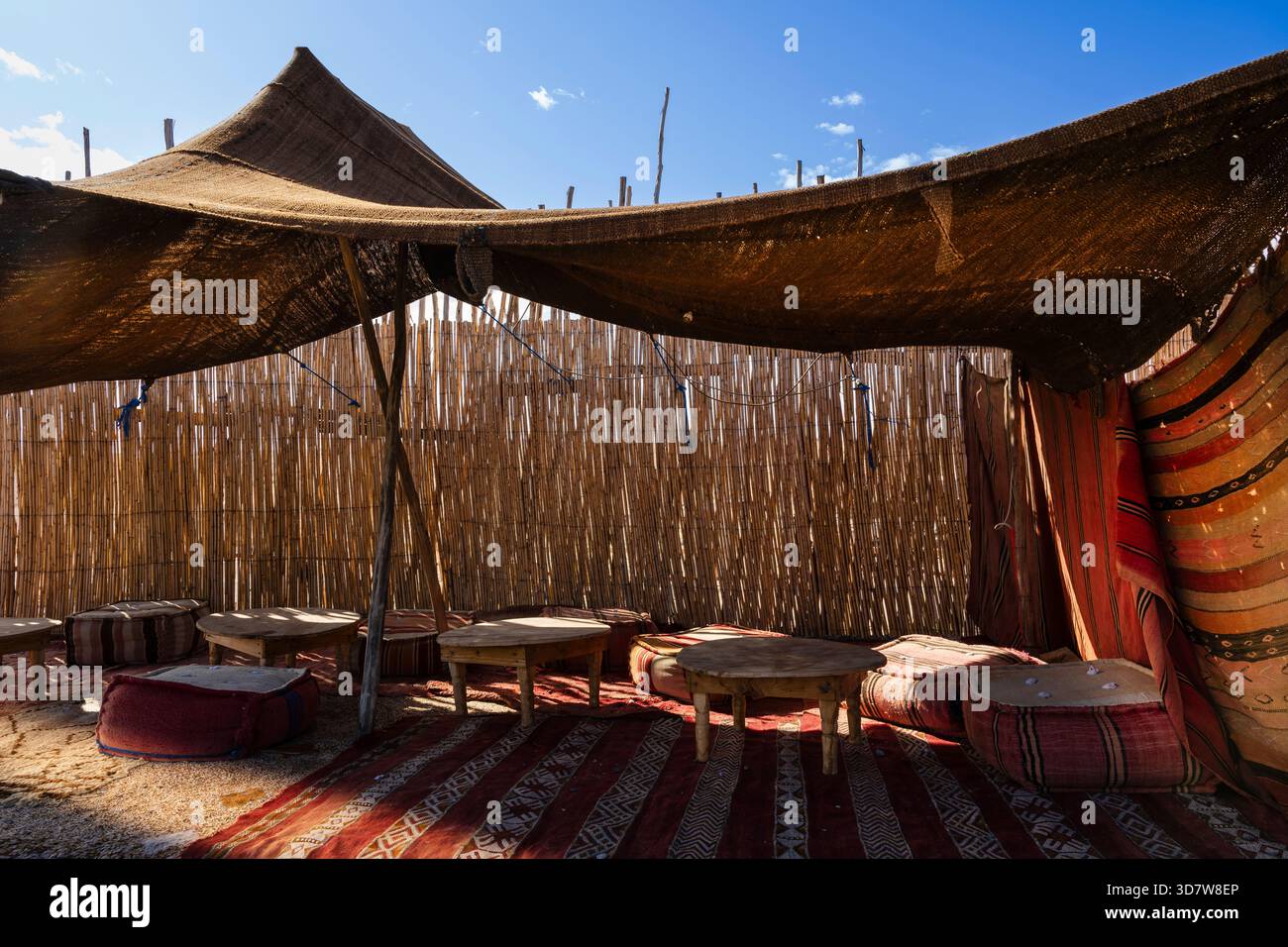 Tradizionale tenda del deserto con tavoli in legno e cuscini colorati sotto un cielo azzurro. Deserto di Agafay, Marrakech-Safi, Marocco Foto Stock
