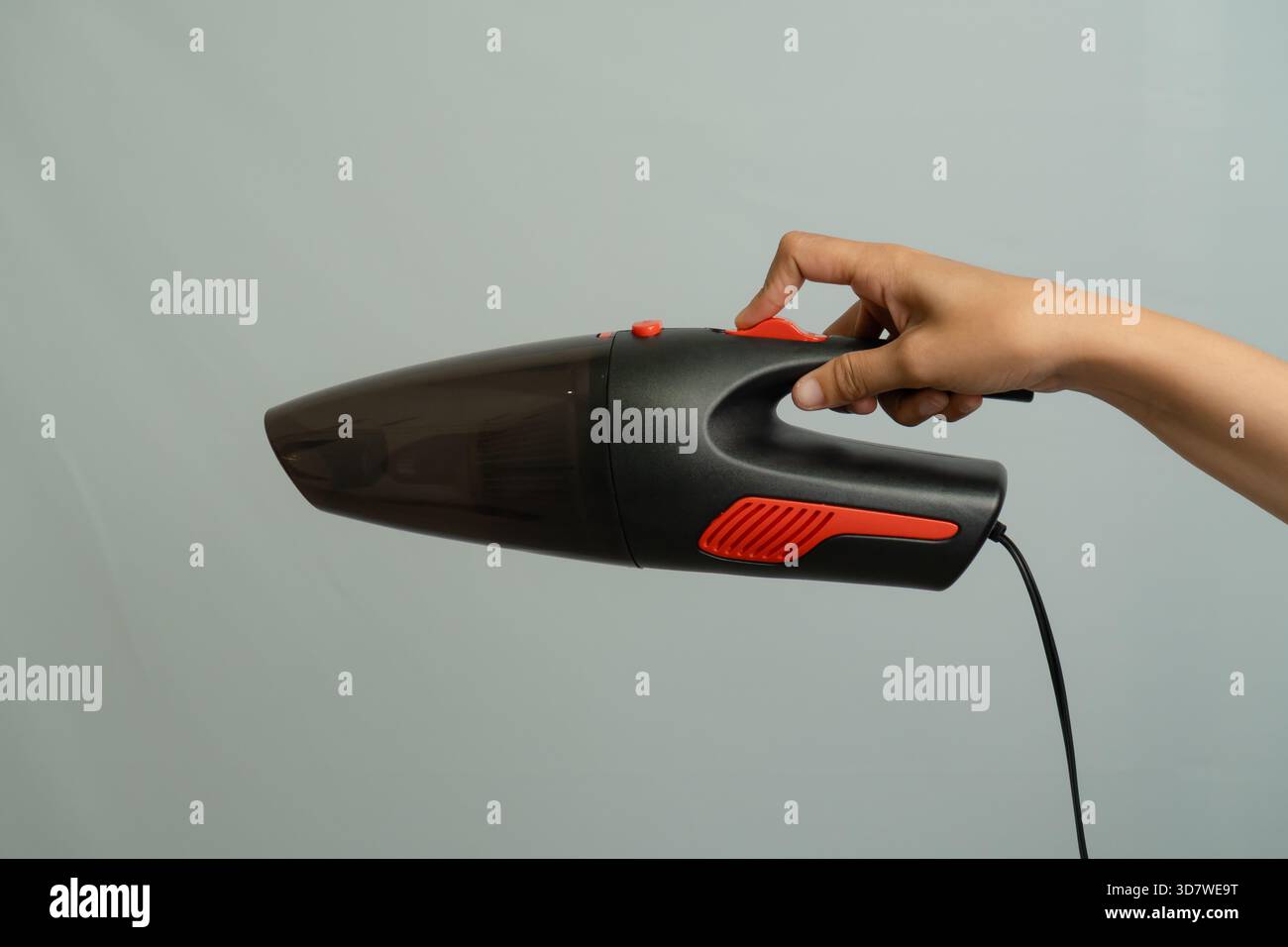 Mano che regge Un aspirapolvere portatile nero con dettagli rossi su sfondo grigio chiaro Foto Stock