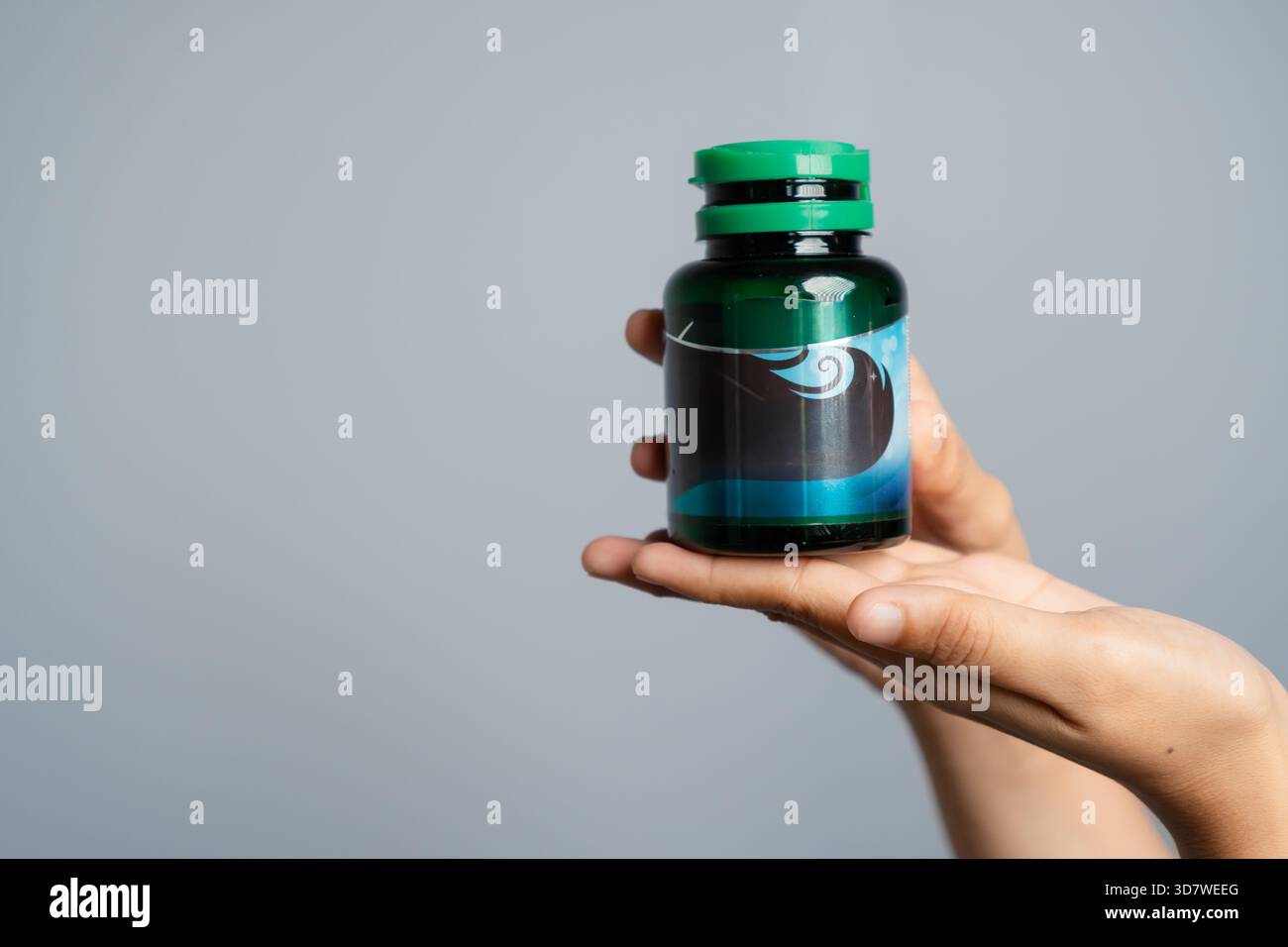 Bottiglia verde per medicinali con supporto a mano con etichetta blu su sfondo grigio Foto Stock