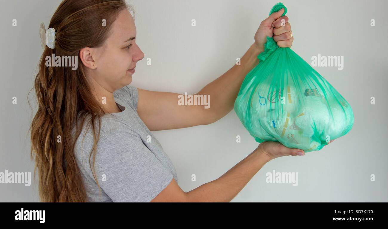Donna che tiene in mano un grande sacchetto verde della spazzatura pieno di pannolini usa e getta usati. Foto Stock