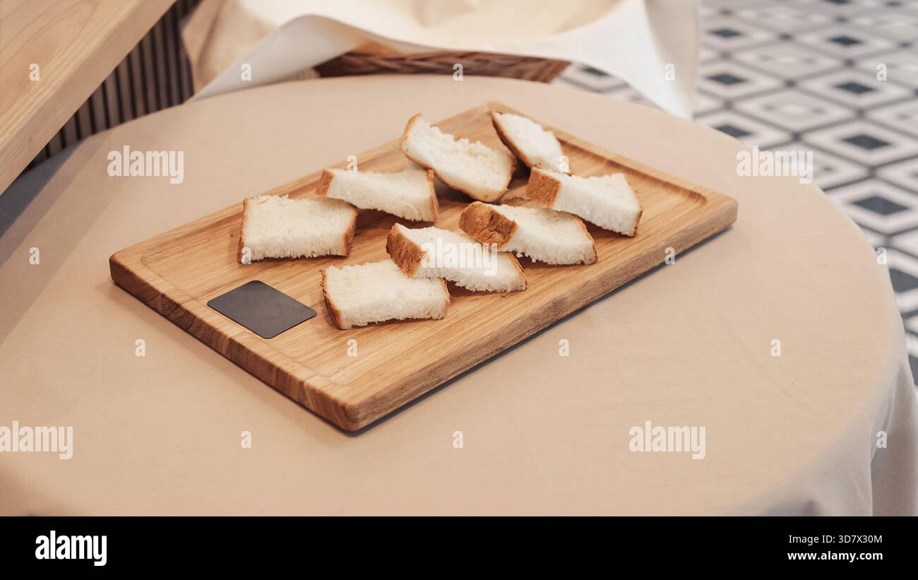 Affettare il pane su un asse di legno. Tagliare irregolarmente pezzi di pane bianco su un piccolo e leggero tavolo da servizio in legno. Foto Stock