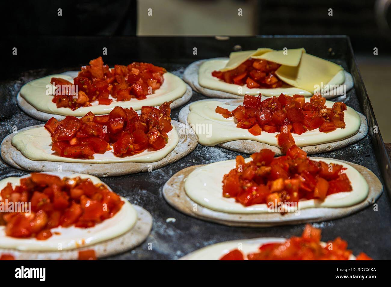 Focaccine fresche disposte su un vassoio, ognuna ricoperta di salsa cremosa e condita con pomodori tritati o paprika in un mercato di Street food natalizio. Foto Stock