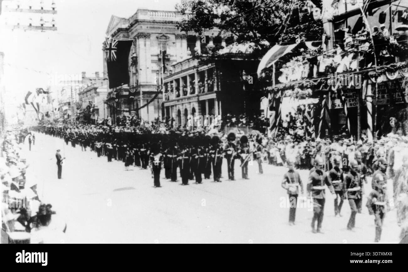 Le truppe imperiali marciano lungo Queen Street, Brisbane, Queensland, 1901. Celebrazioni del Commonwealth australiano. La folla sul sentiero sta guardando le truppe imperiali, vestite con uniformi militari, marciare oltre. Si possono vedere più folle in piedi sulle verande degli edifici della città che costeggiano la strada. Gli edifici sono stati decorati con vari oggetti, tra cui fiori e bandiere, e la bandiera union Jack vola da molti pali di bandiera. Foto Stock