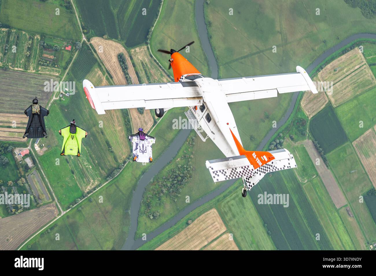 Un aeromobile Technoavia SM-92 Finist STOL vola sopra i terreni agricoli mentre i volanti con tuta alare scivolano in formazione a bordo in caduta libera. Foto Stock